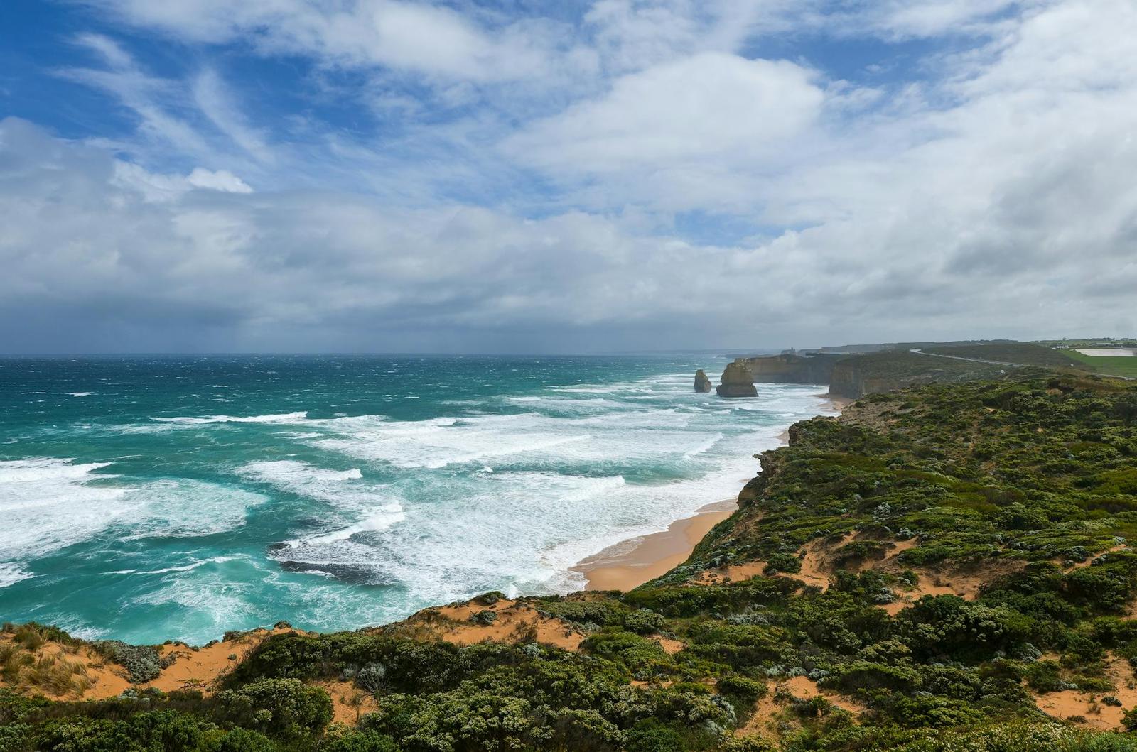 Turquoise waves break along rugged coastal cliffs under a partly cloudy sky