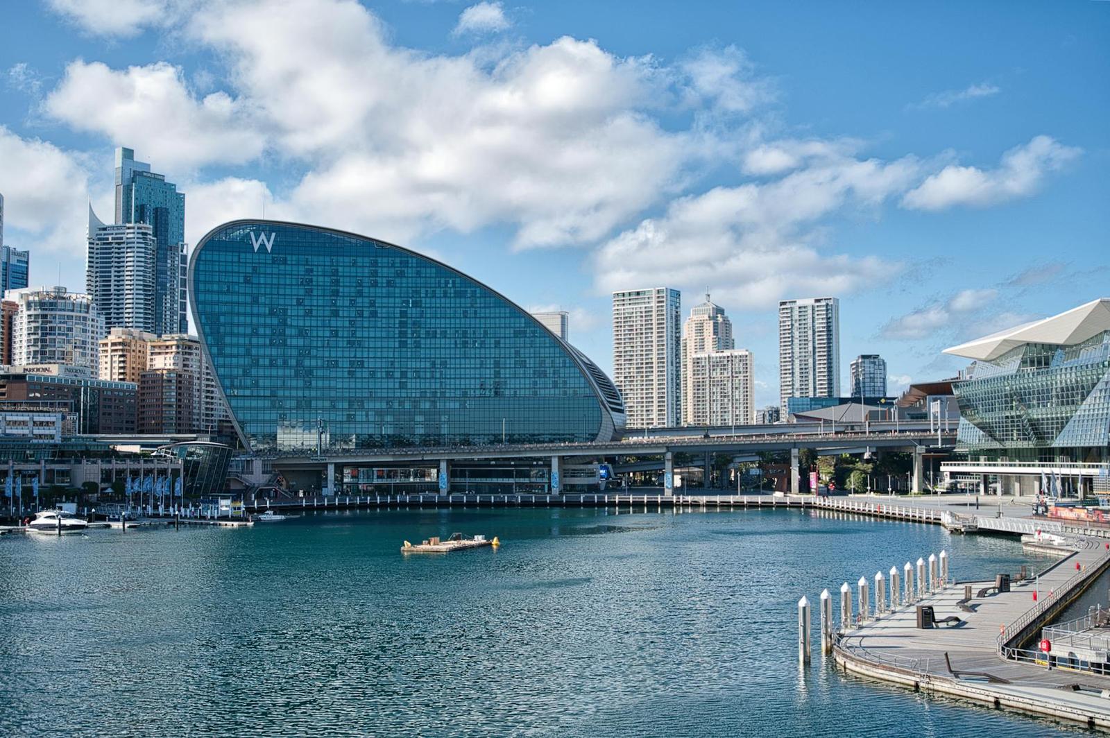 A curved glass waterfront hotel tower among city skyscrapers by the harbour