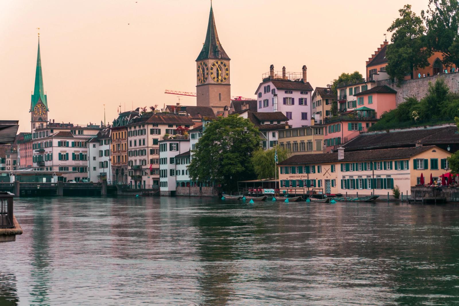 Explore the charming Limmat Riverfront in Zürich with its colorful historic buildings and iconic clock tower at sunset