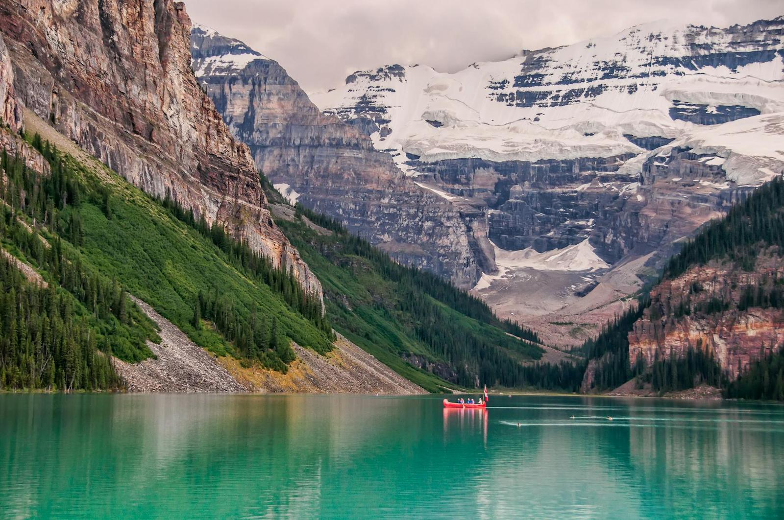 A red canoe crossing a turquoise lake beneath snow-capped peaks and glaciers