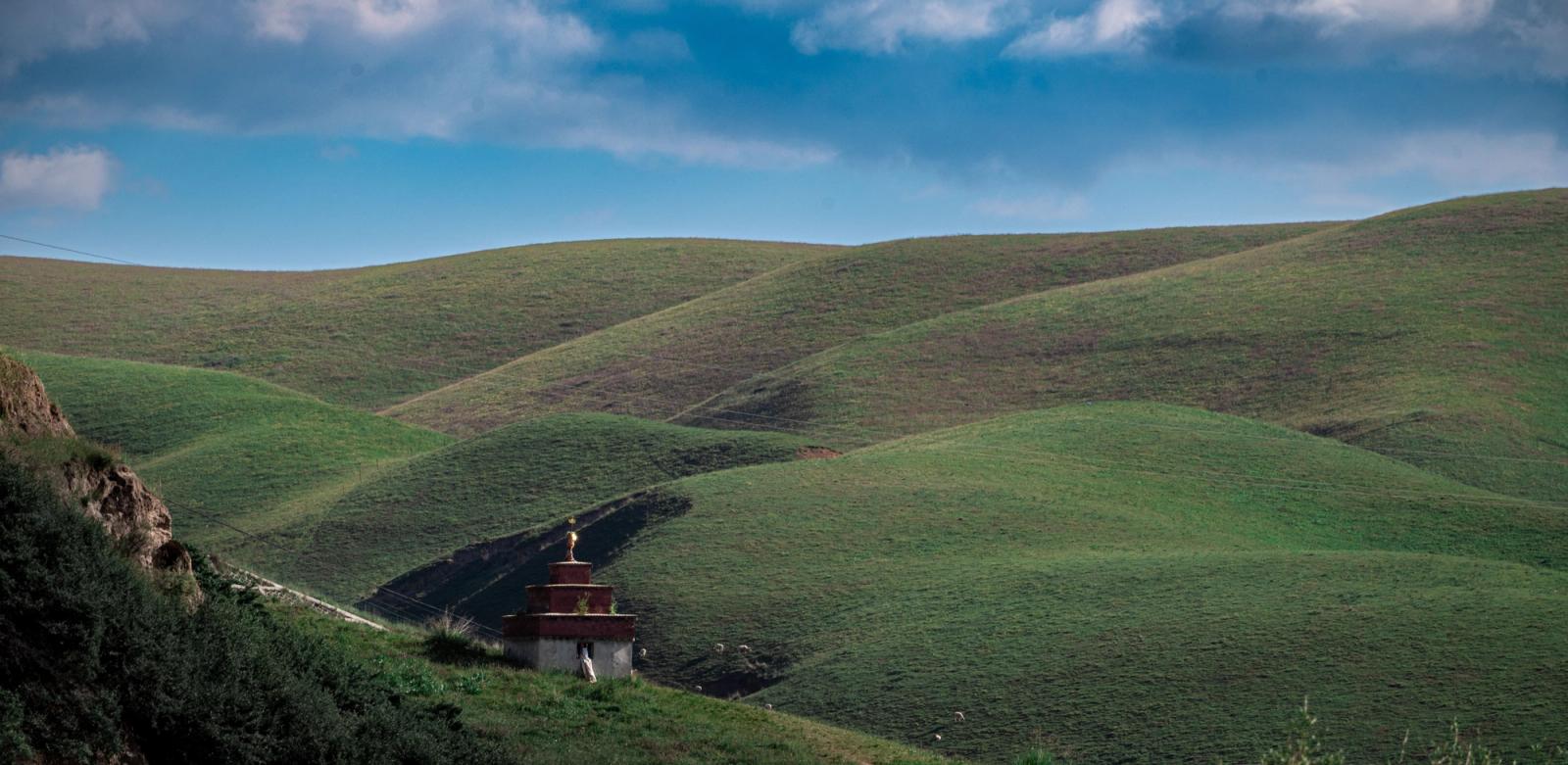 A peaceful landscape of rolling green hills with a solitary Buddhist stupa under a clear blue sky, embodying tranquility