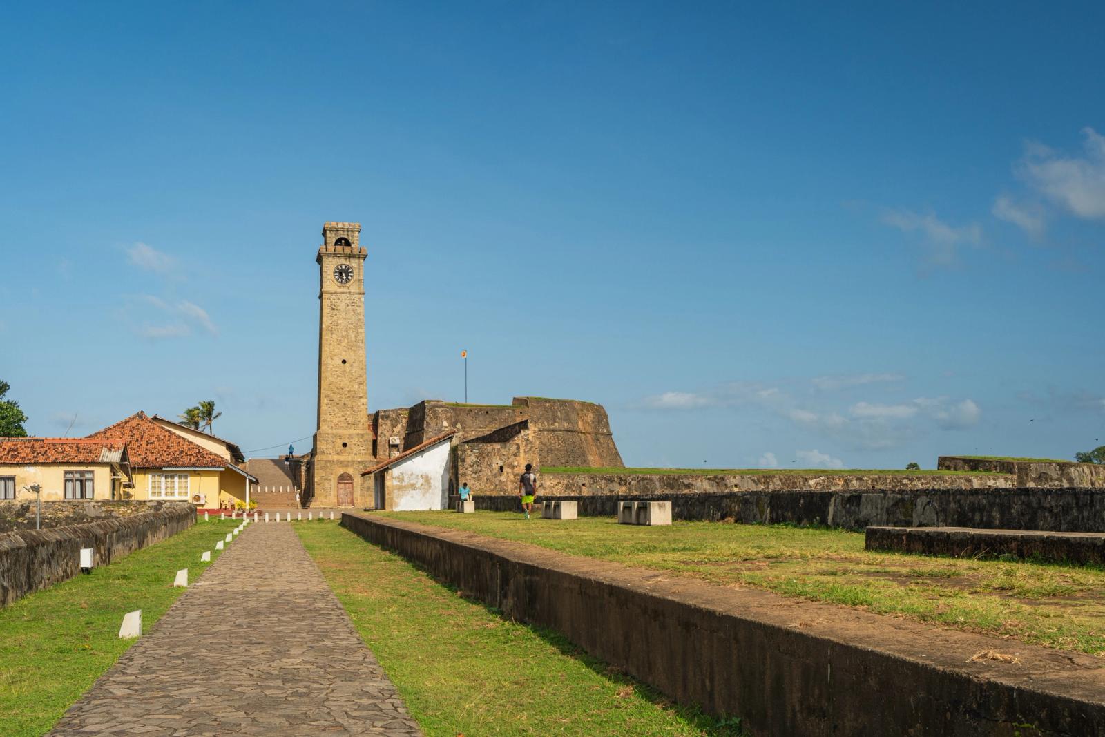 Stone clock tower rising beside old fort ramparts under a clear sky