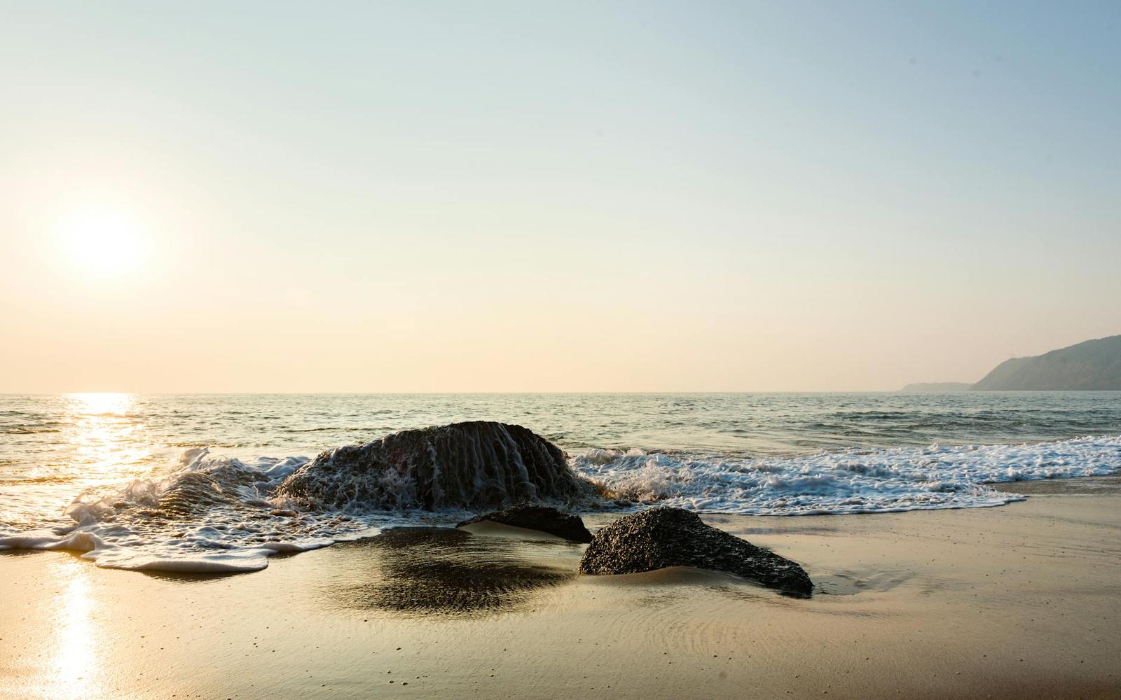 Dark weathered rocks in the surf on a beach at golden hour