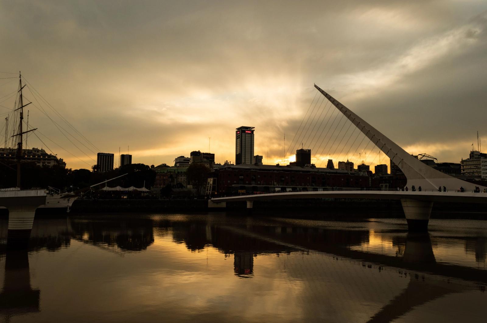 Silhouette of a city skyline with a modern bridge at sunset reflecting in calm waters