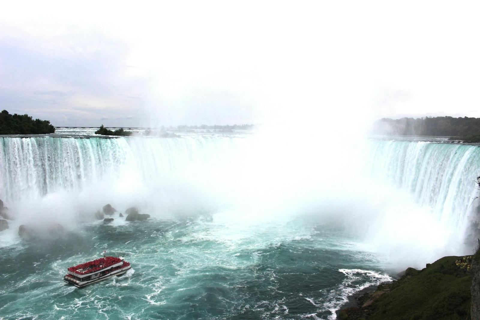 Tour boat approaching a curved waterfall shrouded in mist