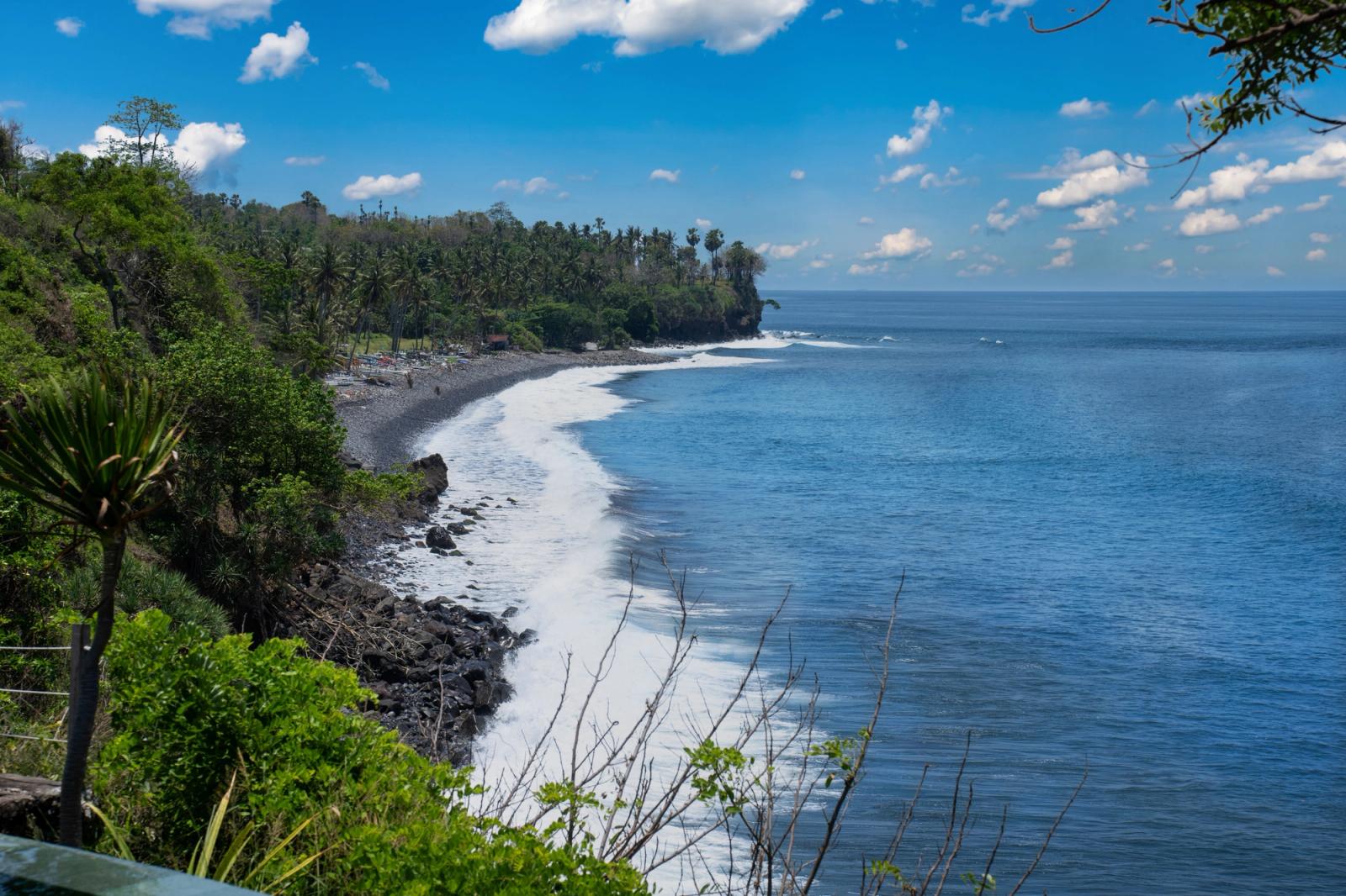 Serene view of Bali's rocky coastline with lush greenery and blue ocean under a vibrant sky