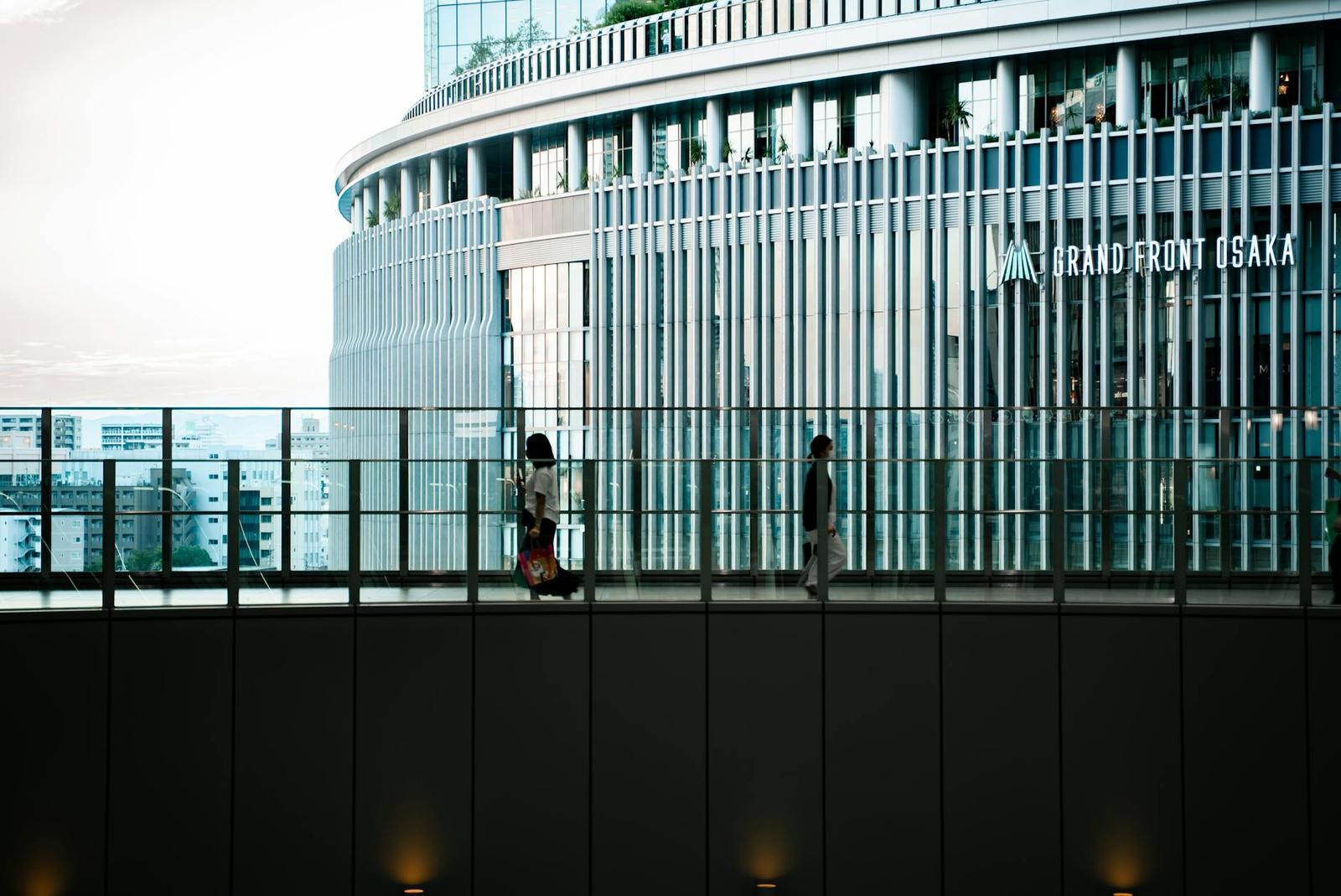 Two people walking along a glass skywalk beside a curved office tower