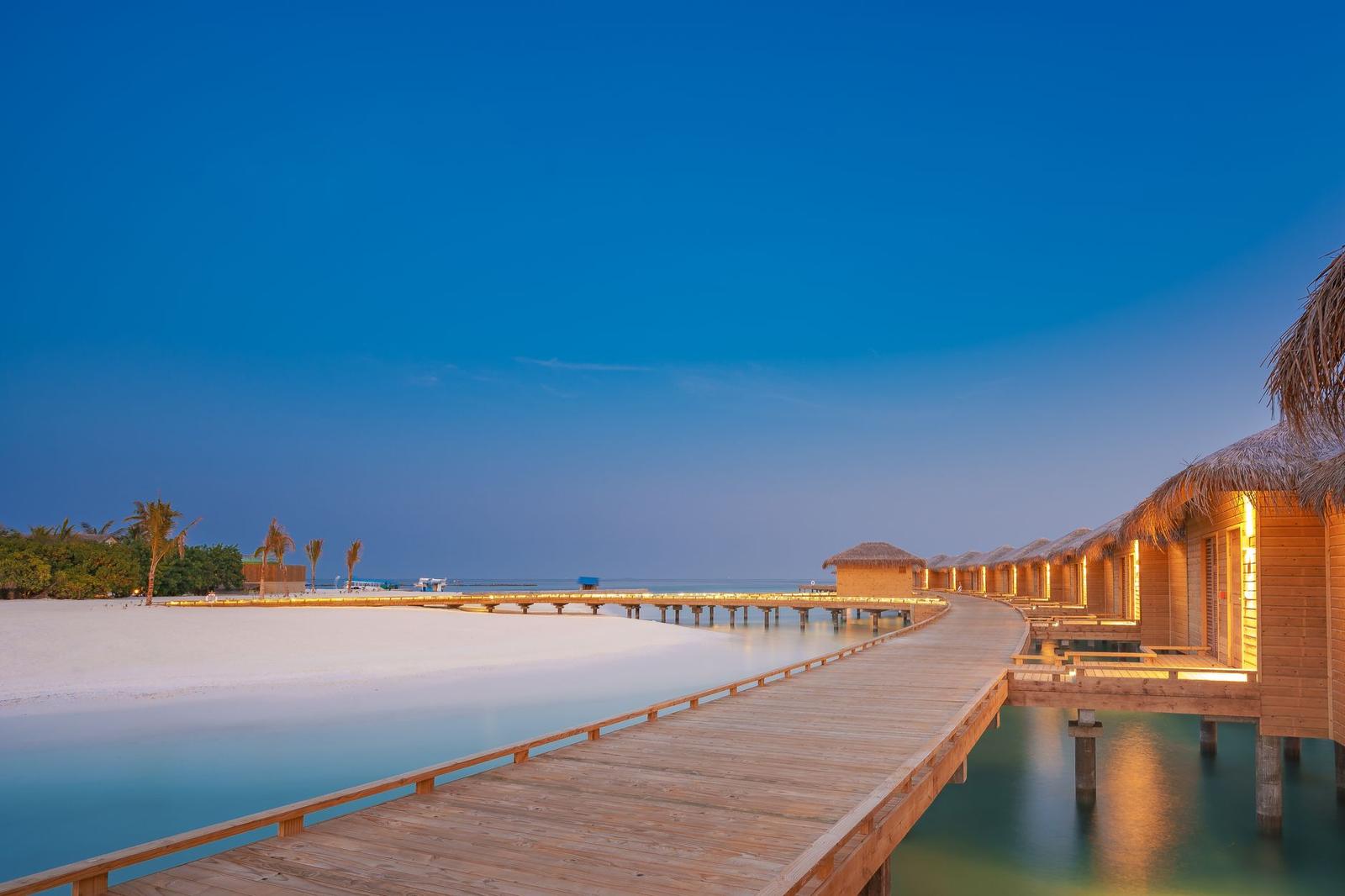 A wooden walkway leading to overwater villas at dusk