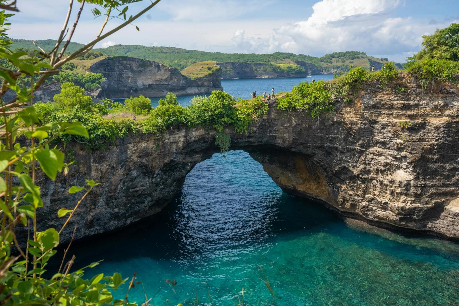 Natural stone arch framing a bright turquoise pool with hills beyond
