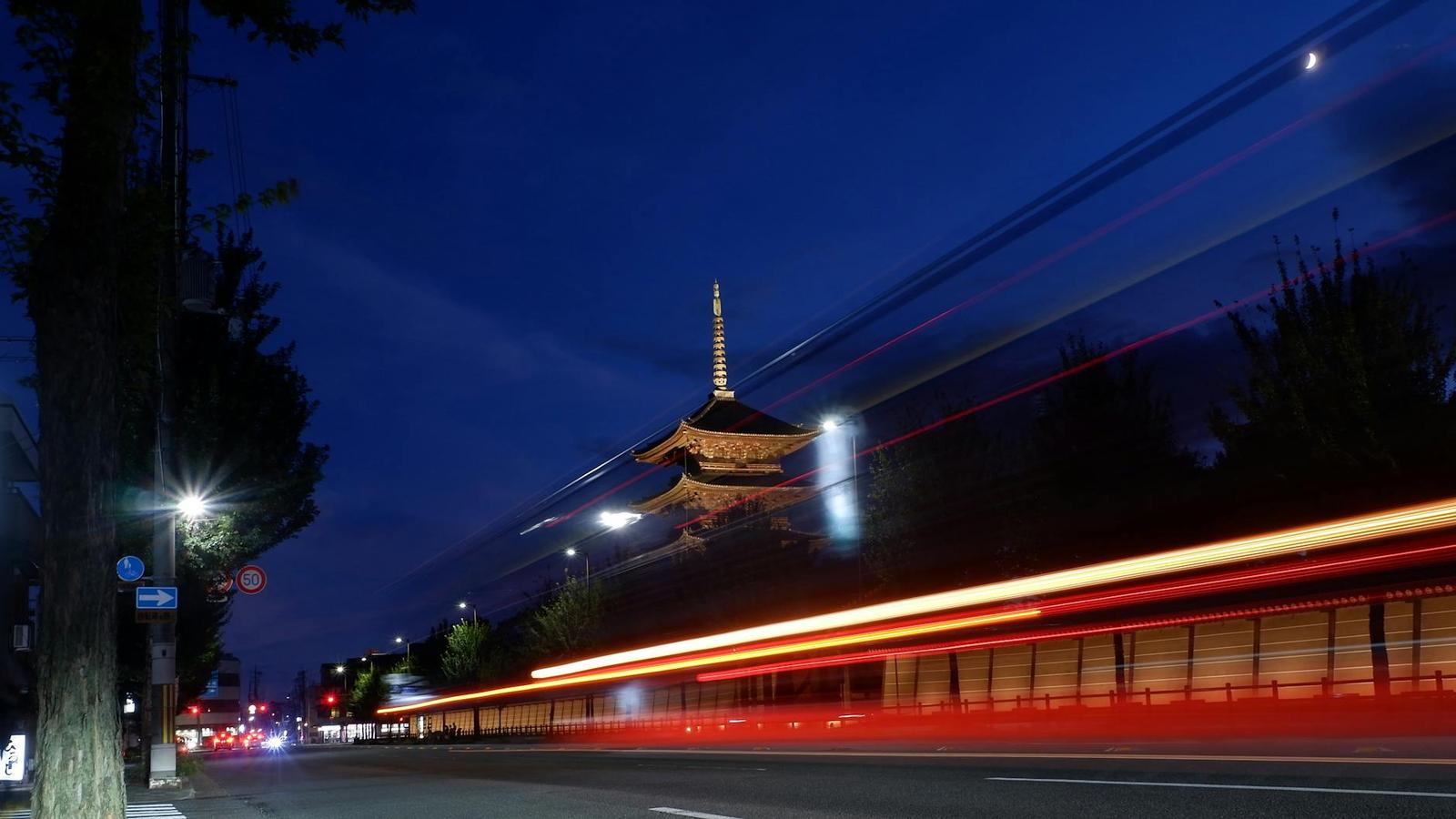 A pagoda silhouetted against dusk with light trails from passing traffic