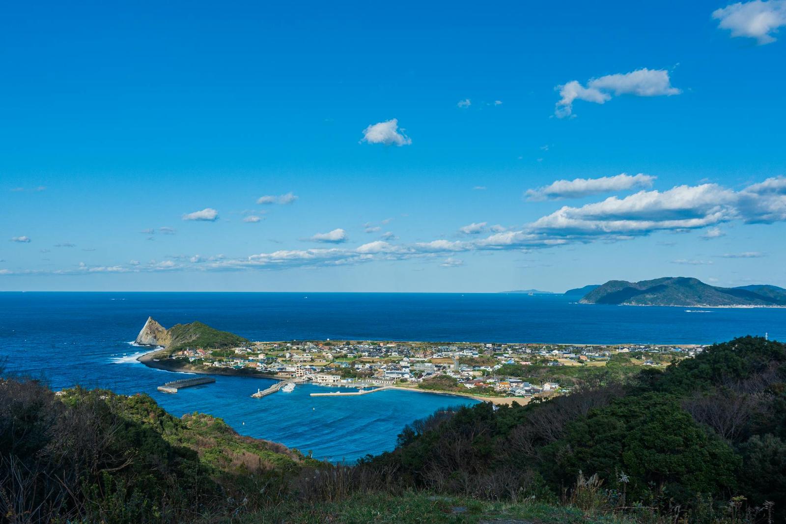 A coastal fishing town seen from a hilltop above a blue bay