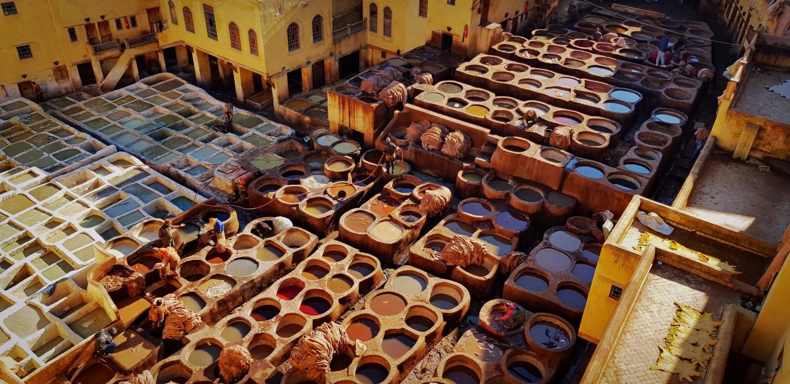 Rows of round stone dye pits filled with coloured liquid at an open-air tannery