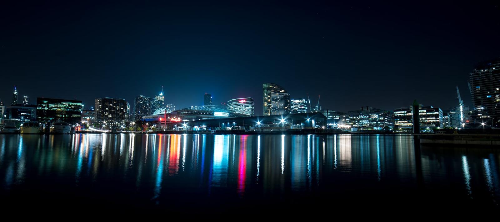 Colourful lights of a city skyline reflected across a dark harbour at night
