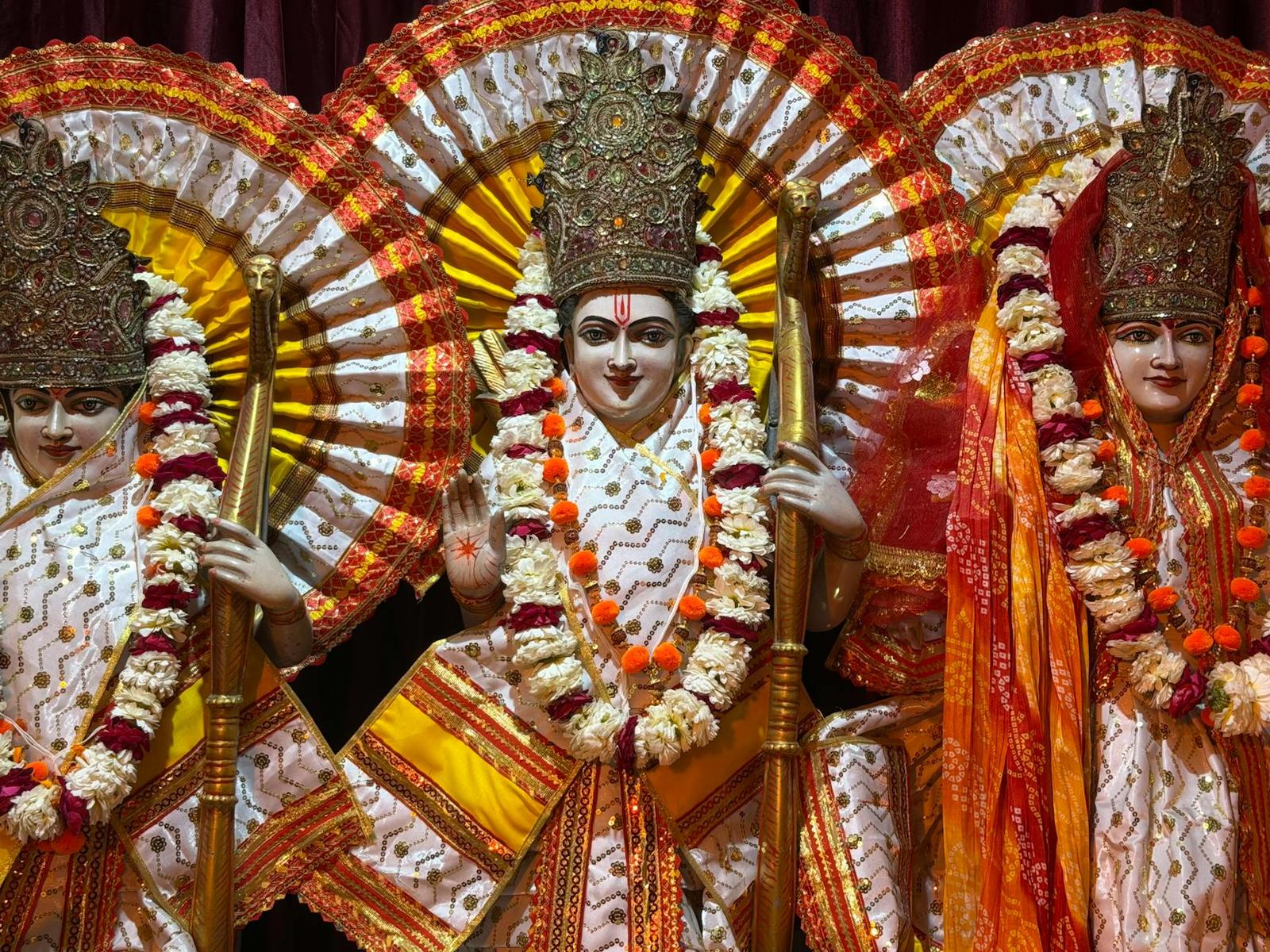 Three ornately garlanded deity statues with radiant crown backdrops