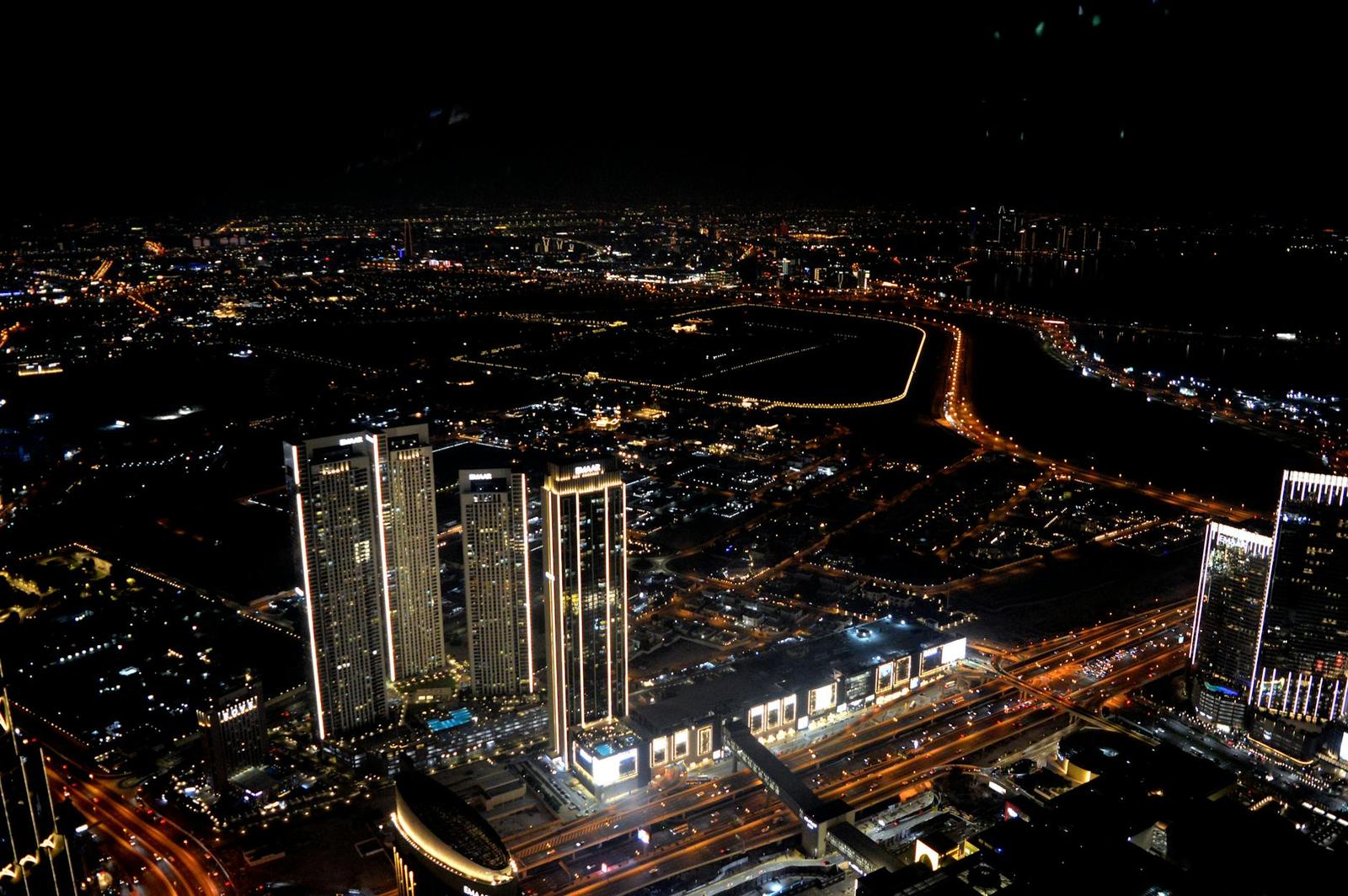 A lit-up city skyline at night with towers along a curved waterfront road