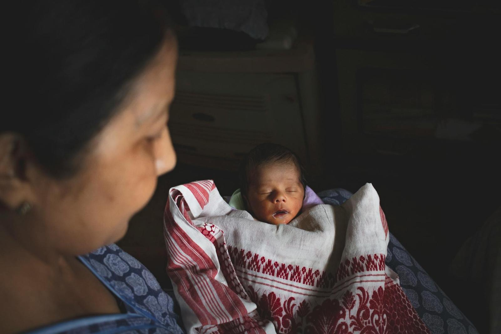 A woman gazes at a newborn wrapped in a traditional patterned cloth