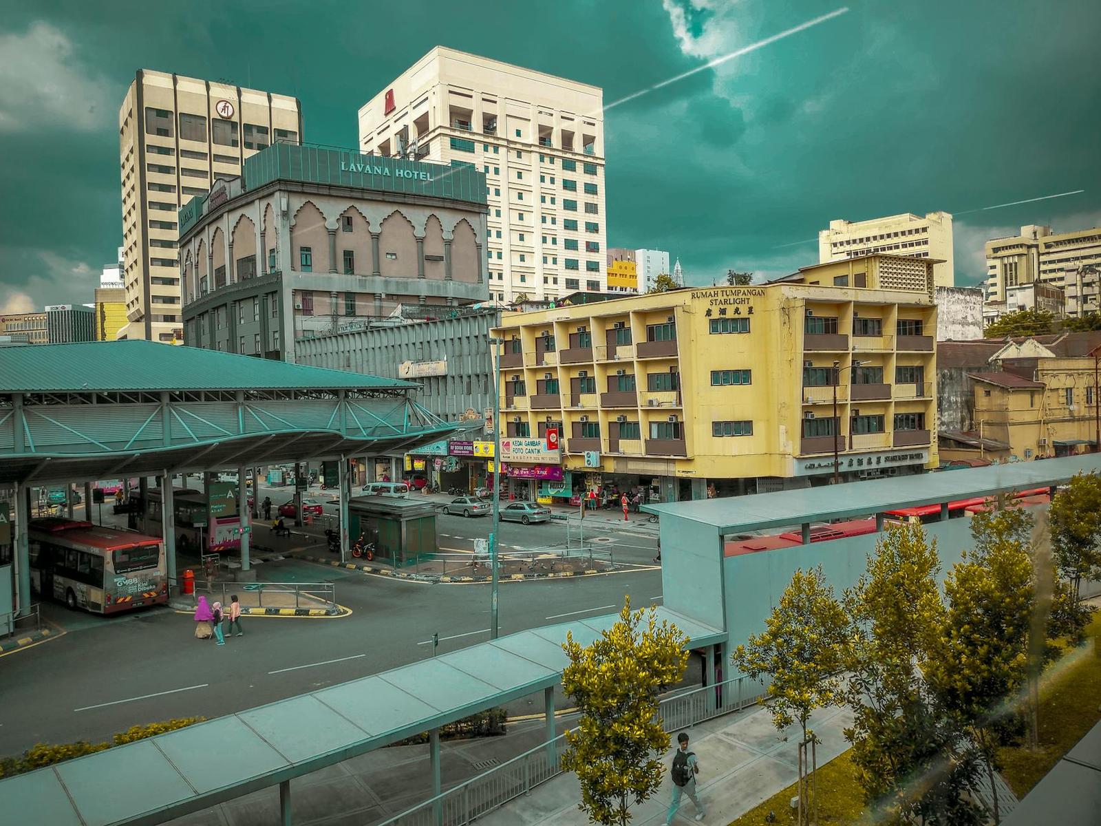 A city street with a bus terminal and illuminated buildings under a teal sky