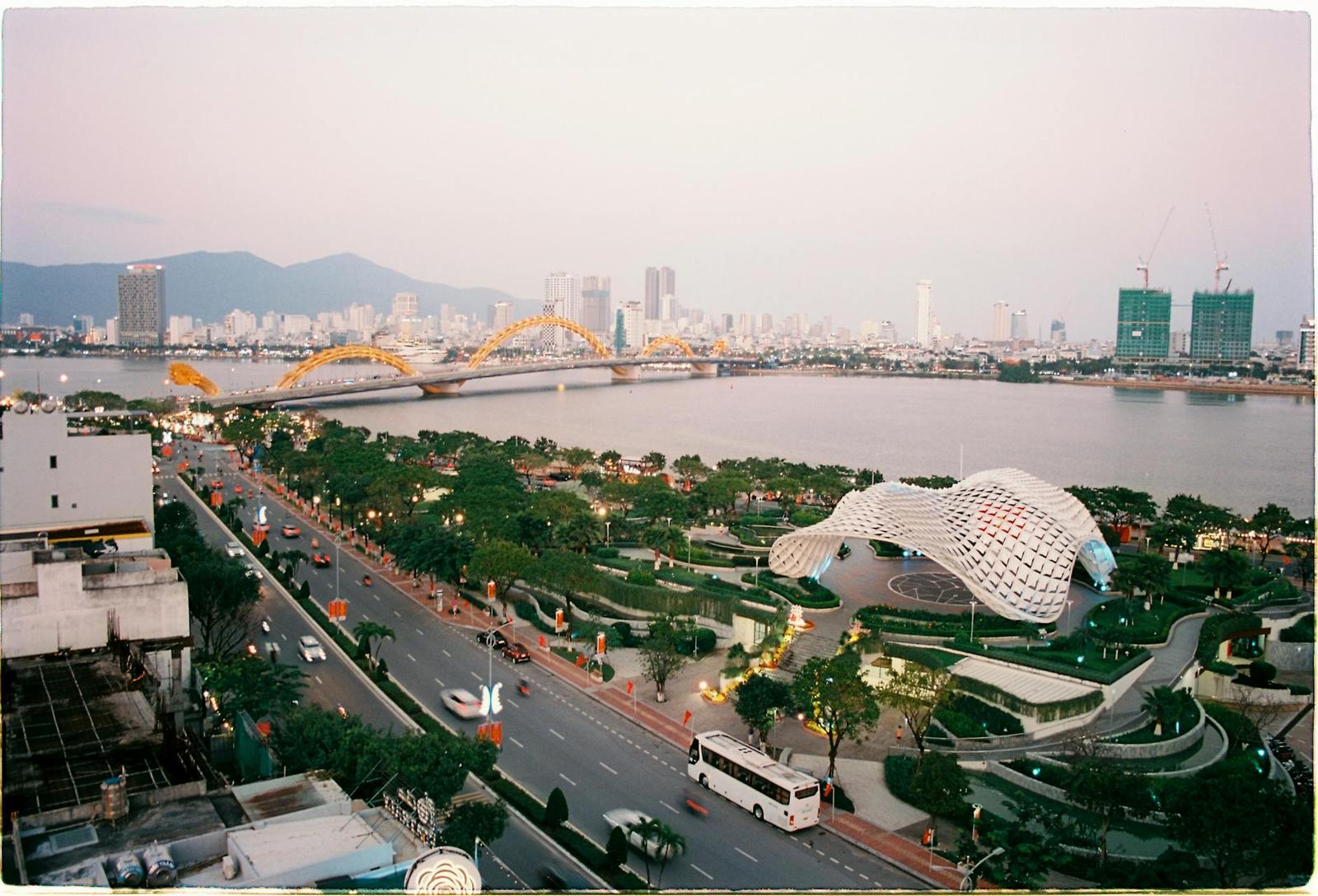 Elevated view of a riverside boulevard with a curved bridge and a domed lattice building at dusk