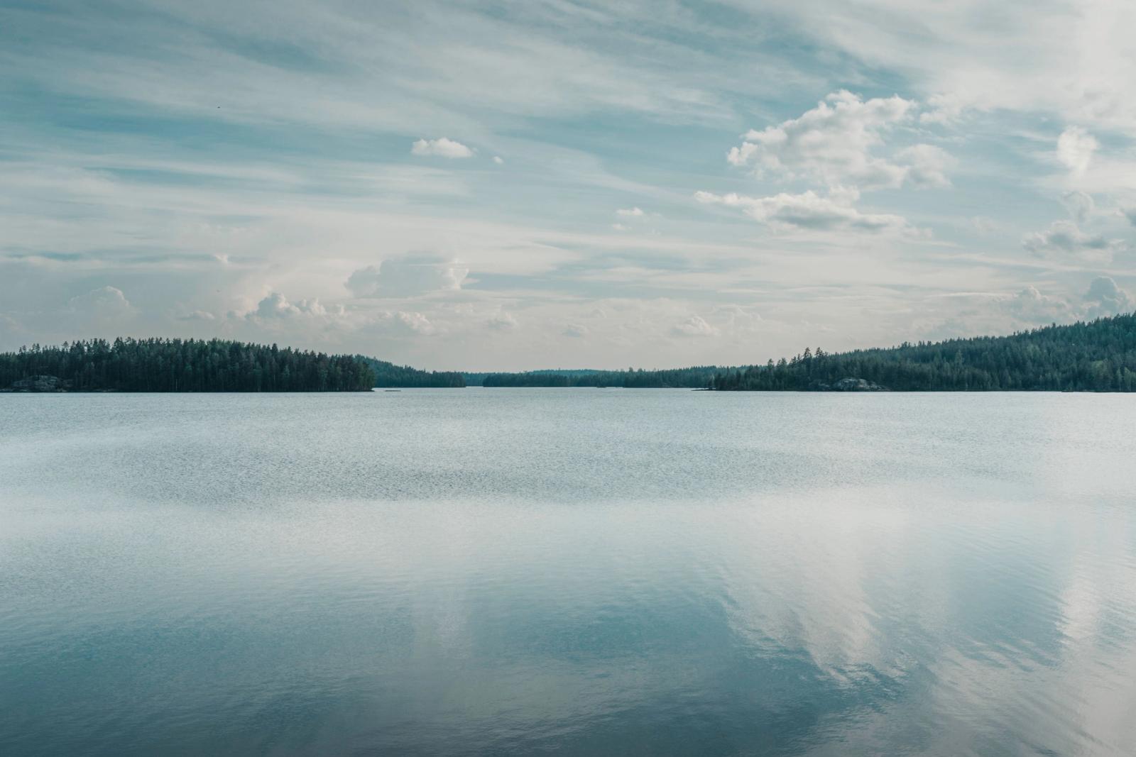 Peaceful lake scene in Finland with reflections on water under a cloudy sky. Captures tranquility and natural beauty