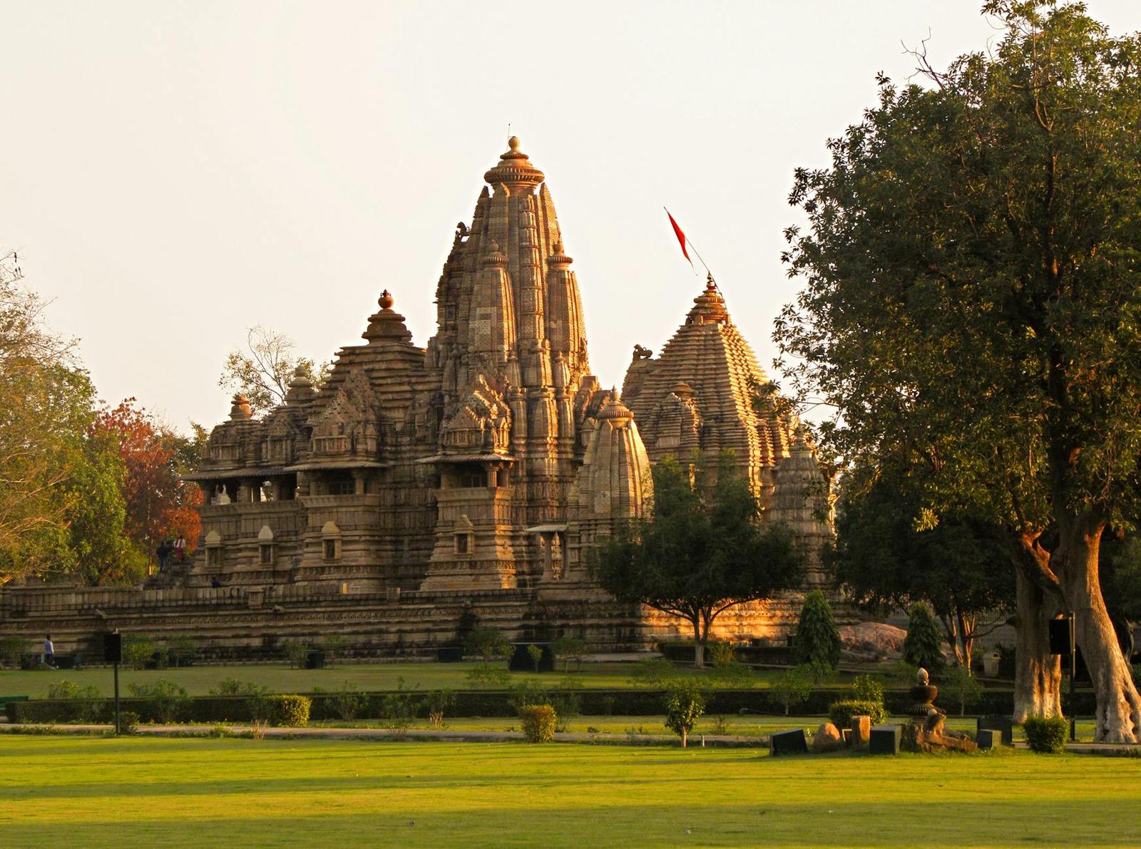 An ornately carved stone temple with a tall spire amid green lawns