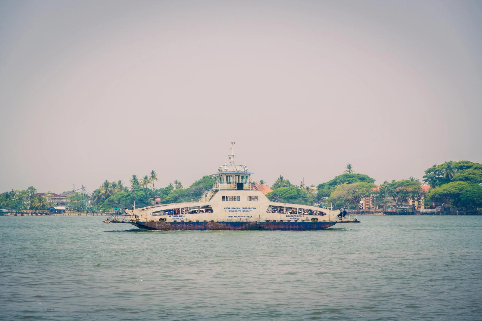 A vintage ferry navigates along a tropical coastline near Kochi, showcasing serene coastal vibes