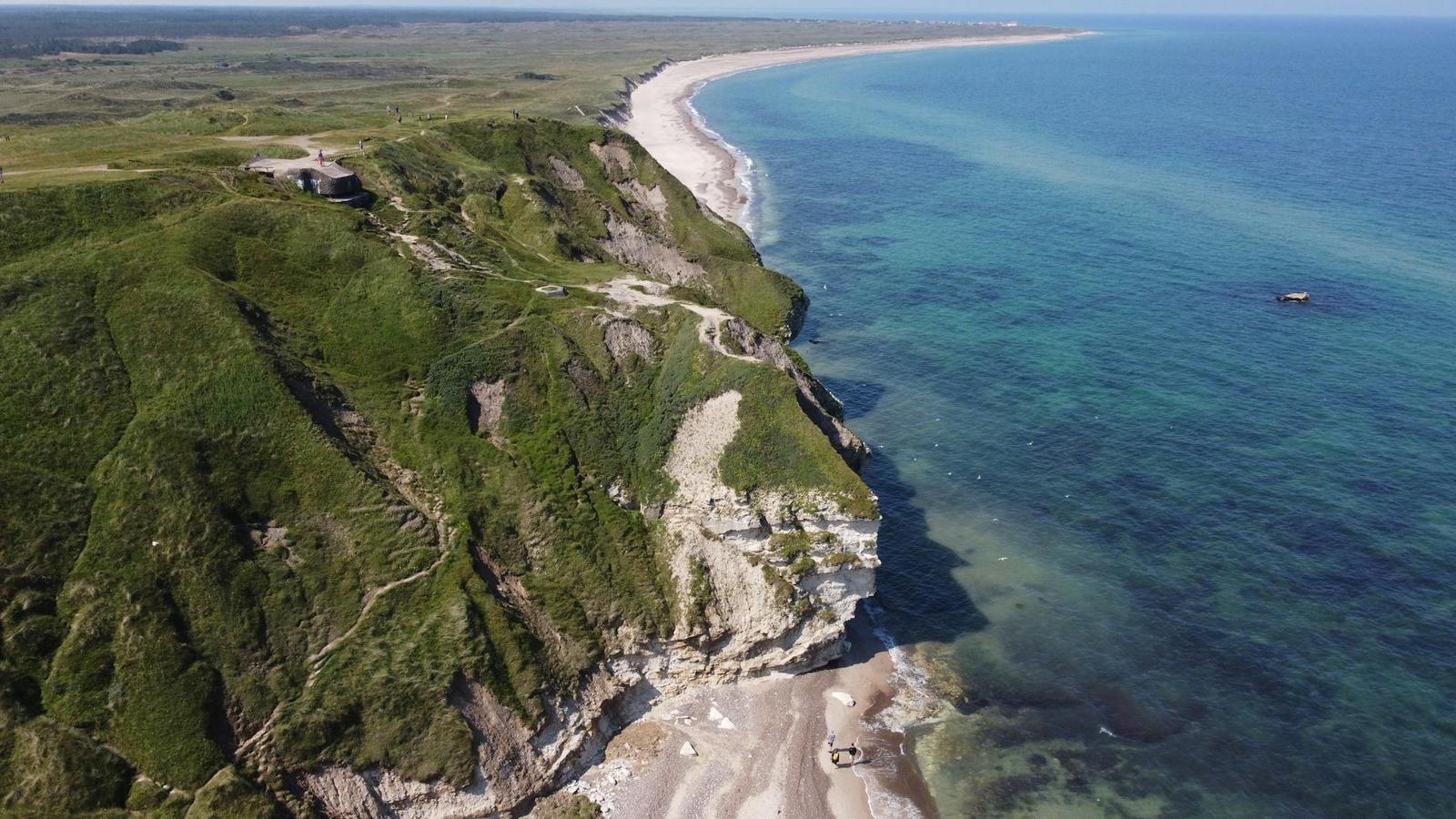 Aerial view of grassy cliffs meeting a turquoise coastline