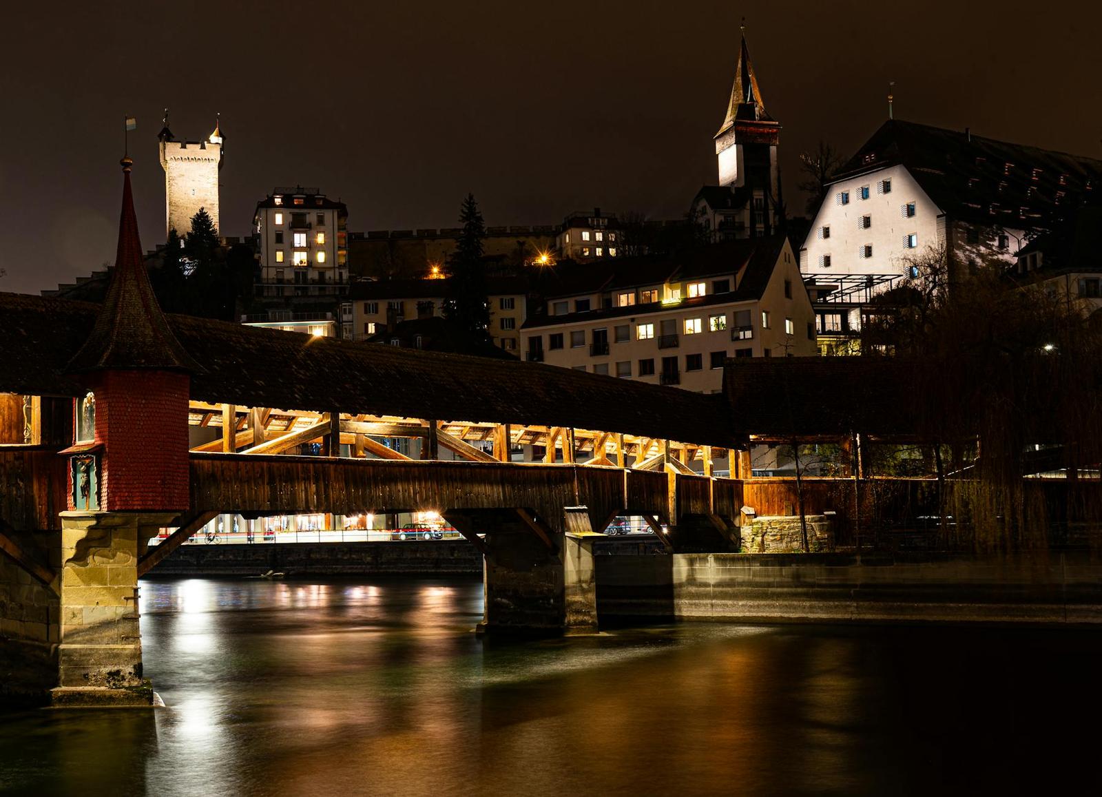 Covered wooden bridge lit up at night beside stone towers