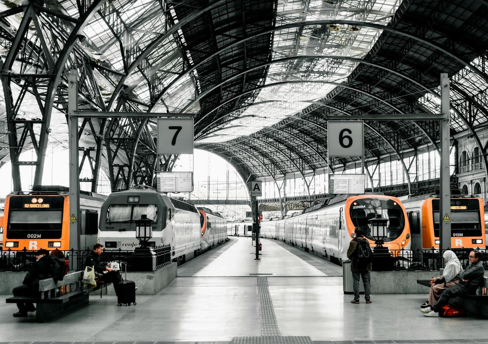Ornate glass and iron train station roof over orange trains and waiting travelers