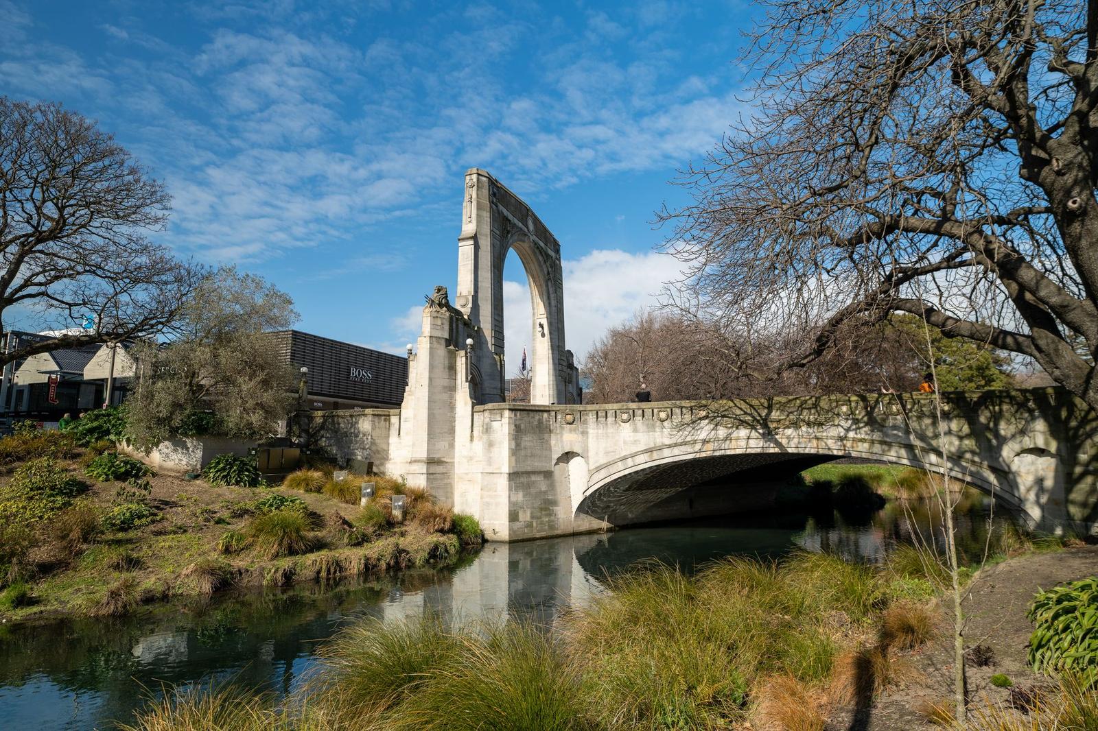A stone memorial bridge arching over a calm river lined with trees