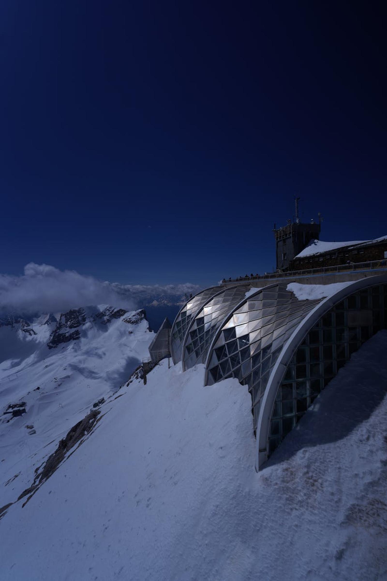 Glass-domed mountain station overlooking a sea of snow at dusk