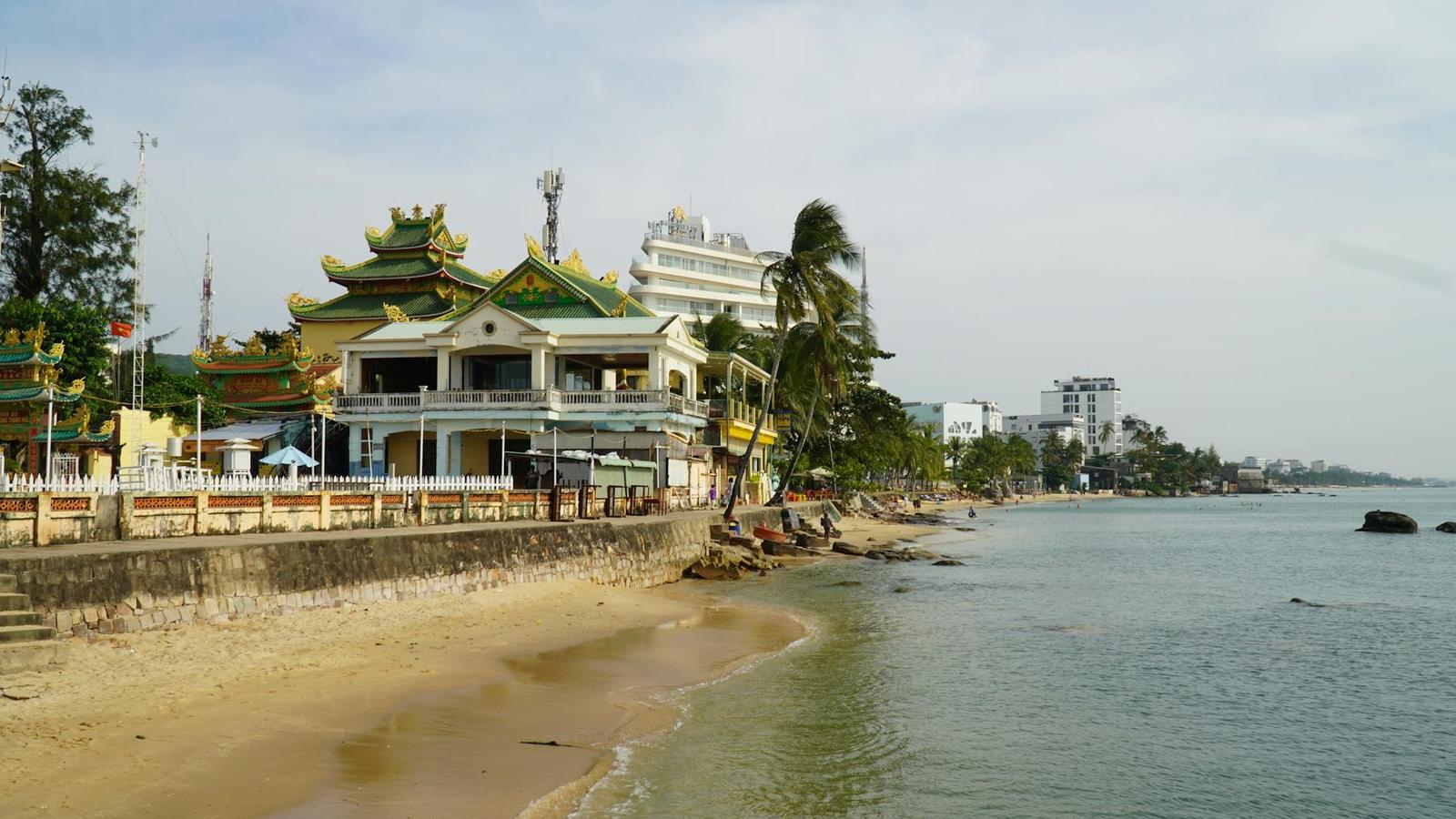 Coastal promenade with an ornate pagoda roof beside a sandy beach