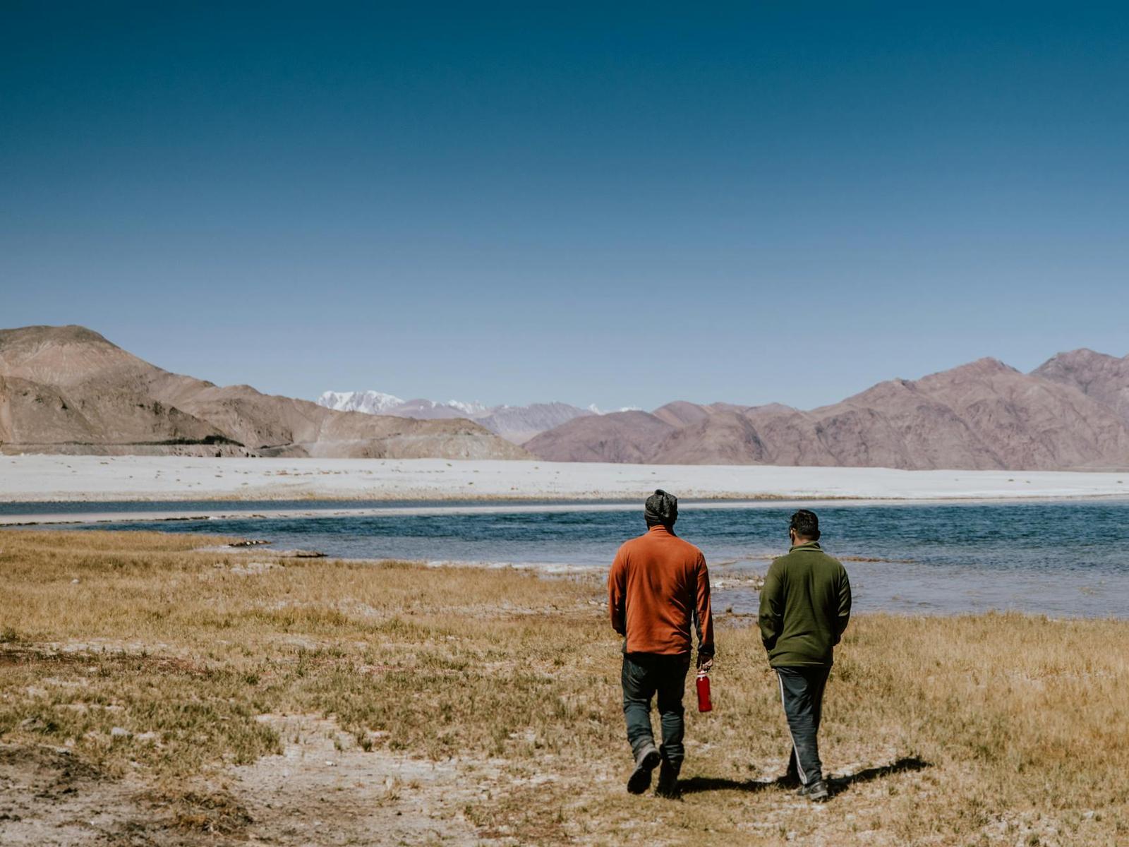 Two men walking along a dry lakeshore toward distant snow-dusted mountains