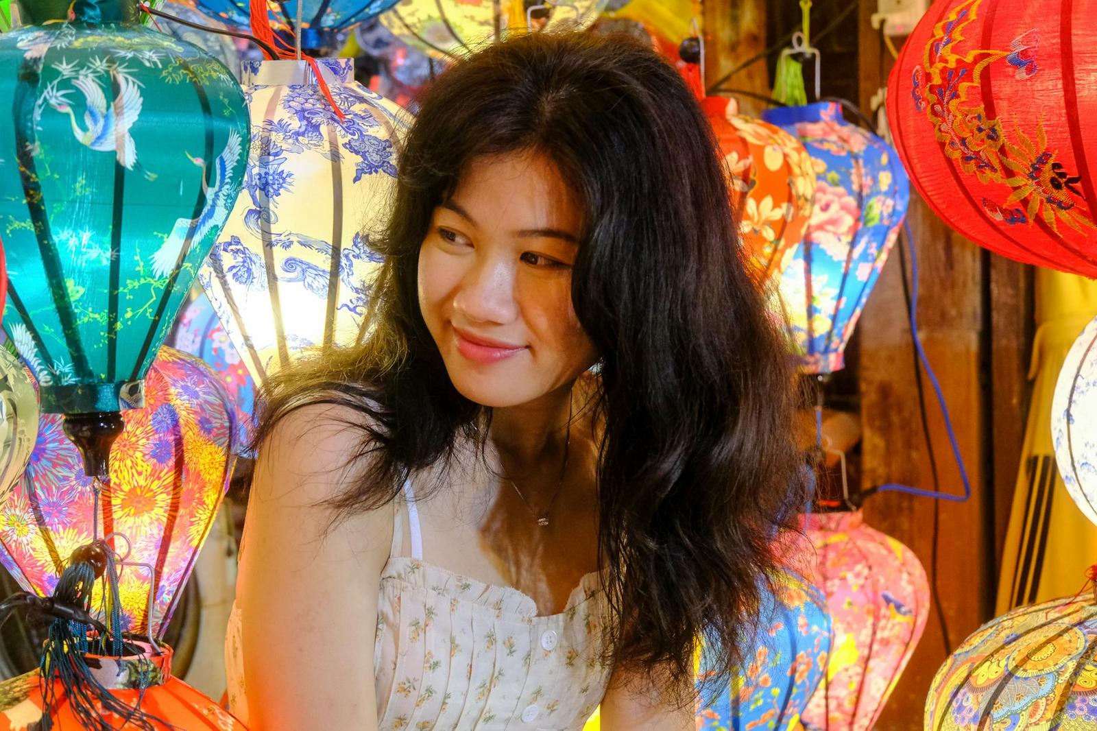 A close-up of a woman smiling among rows of colorful hanging silk lanterns