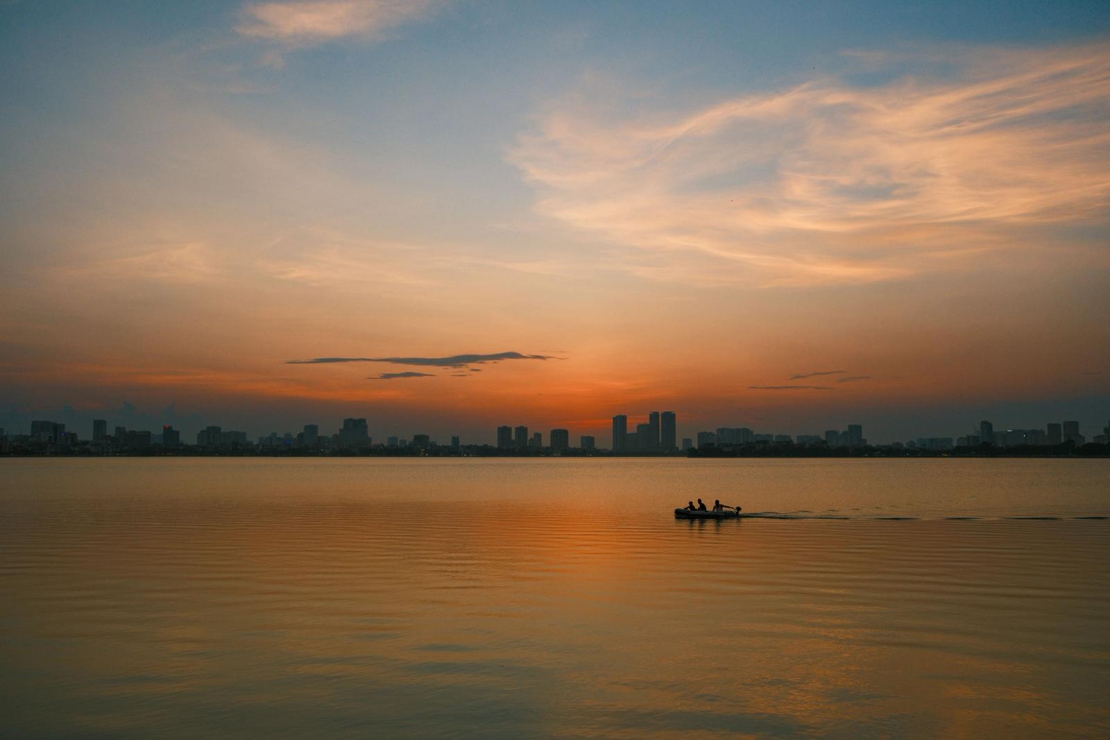Tranquil sunset view of a boat on West Lake, Hanoi, Vietnam, with city skyline