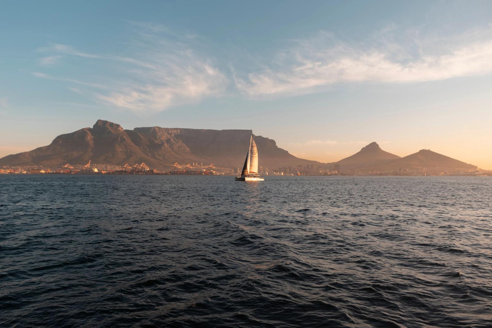 Sailboat navigating the ocean with Table Mountain and Cape Town in the backdrop during a serene sunset