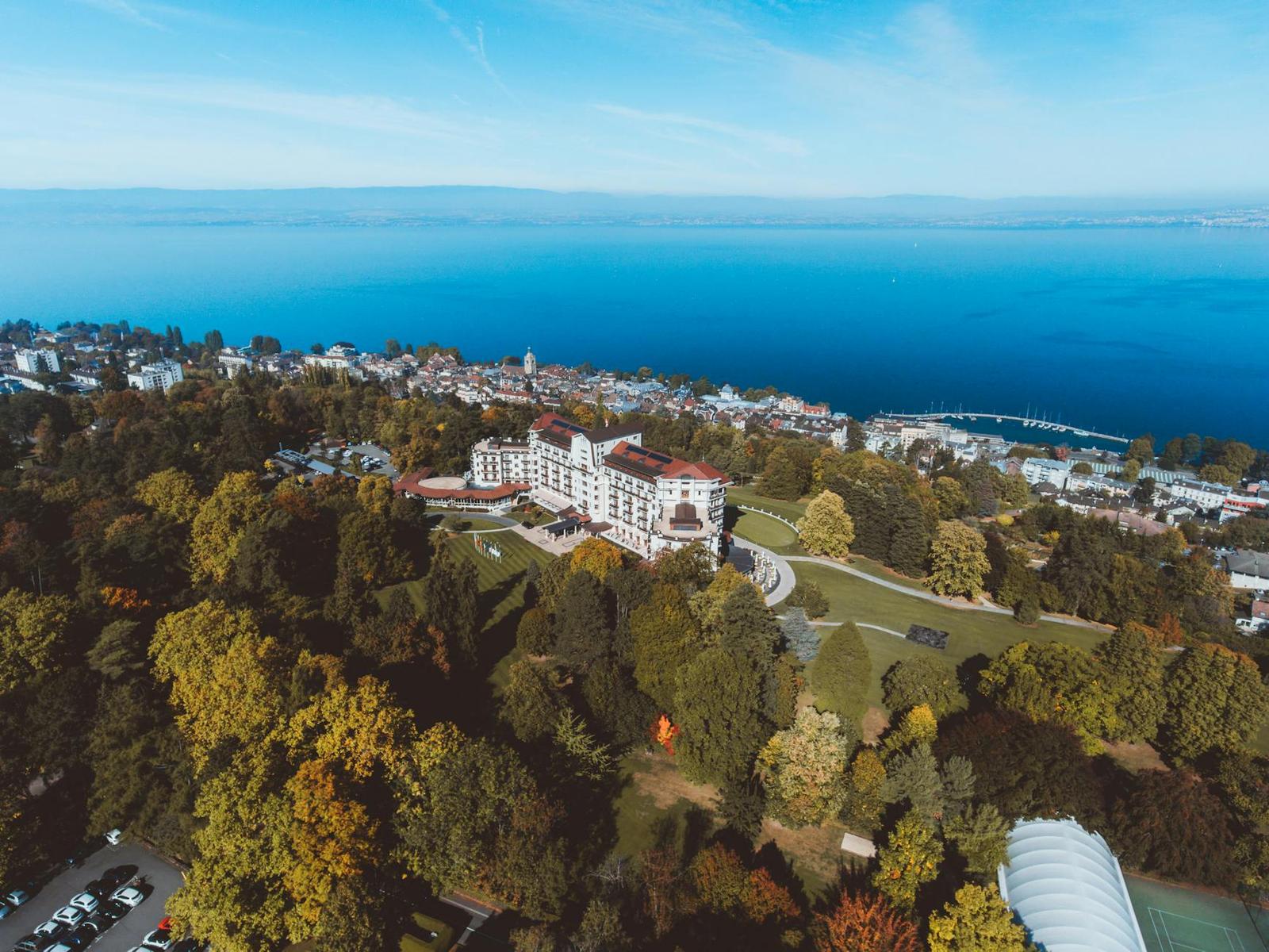 Aerial view of a grand hilltop hotel overlooking a wooded lakeside town
