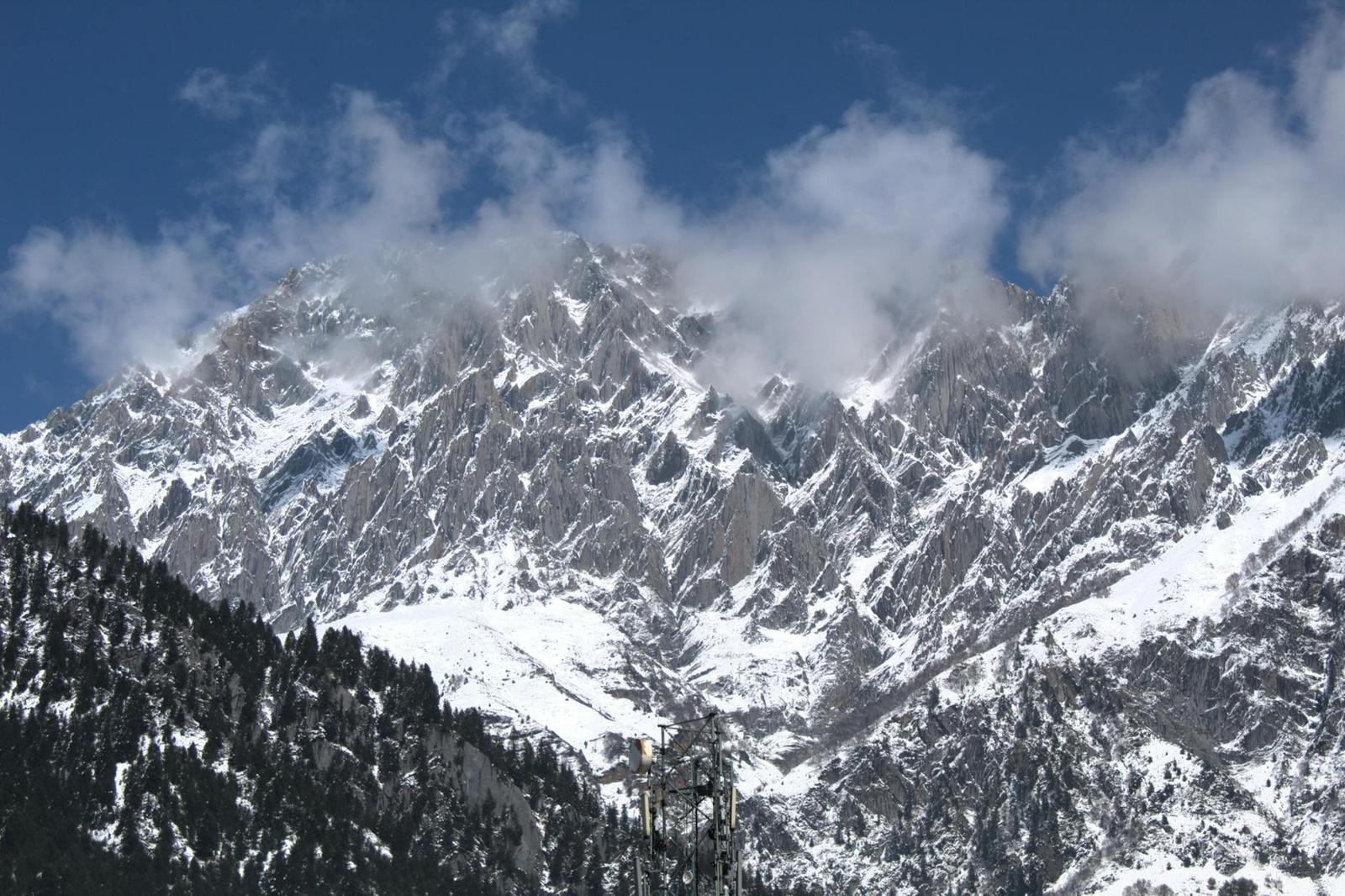 Jagged snow covered peaks wreathed in cloud above a pine forest