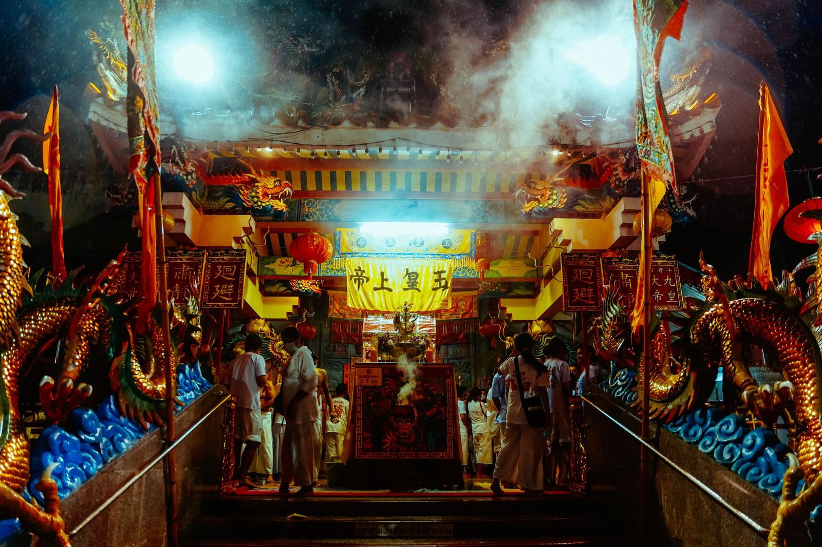 Worshippers at a smoke-filled temple shrine flanked by golden dragon statues at night