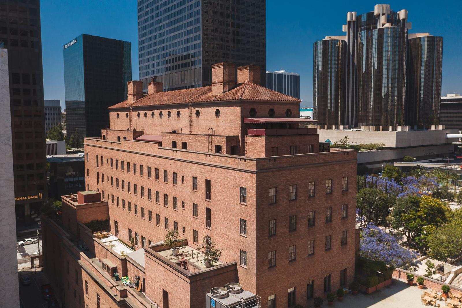 A red brick hotel building with a terraced rooftop garden among downtown skyscrapers