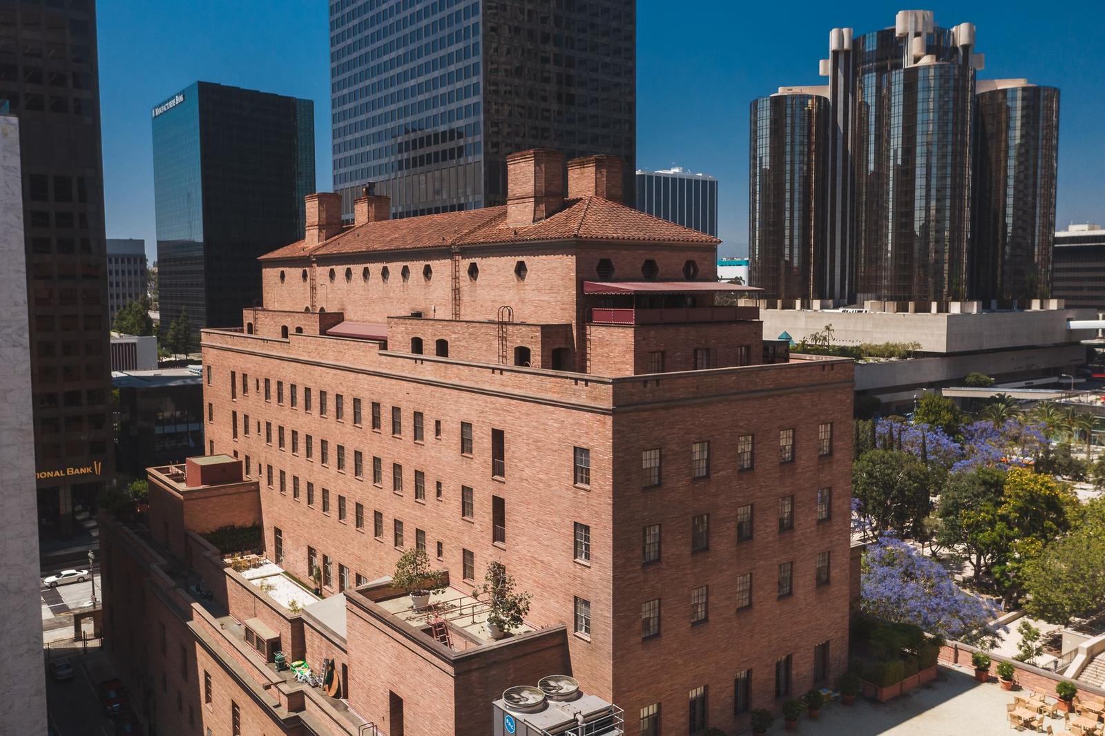 A red brick hotel building with a terraced rooftop garden among downtown skyscrapers