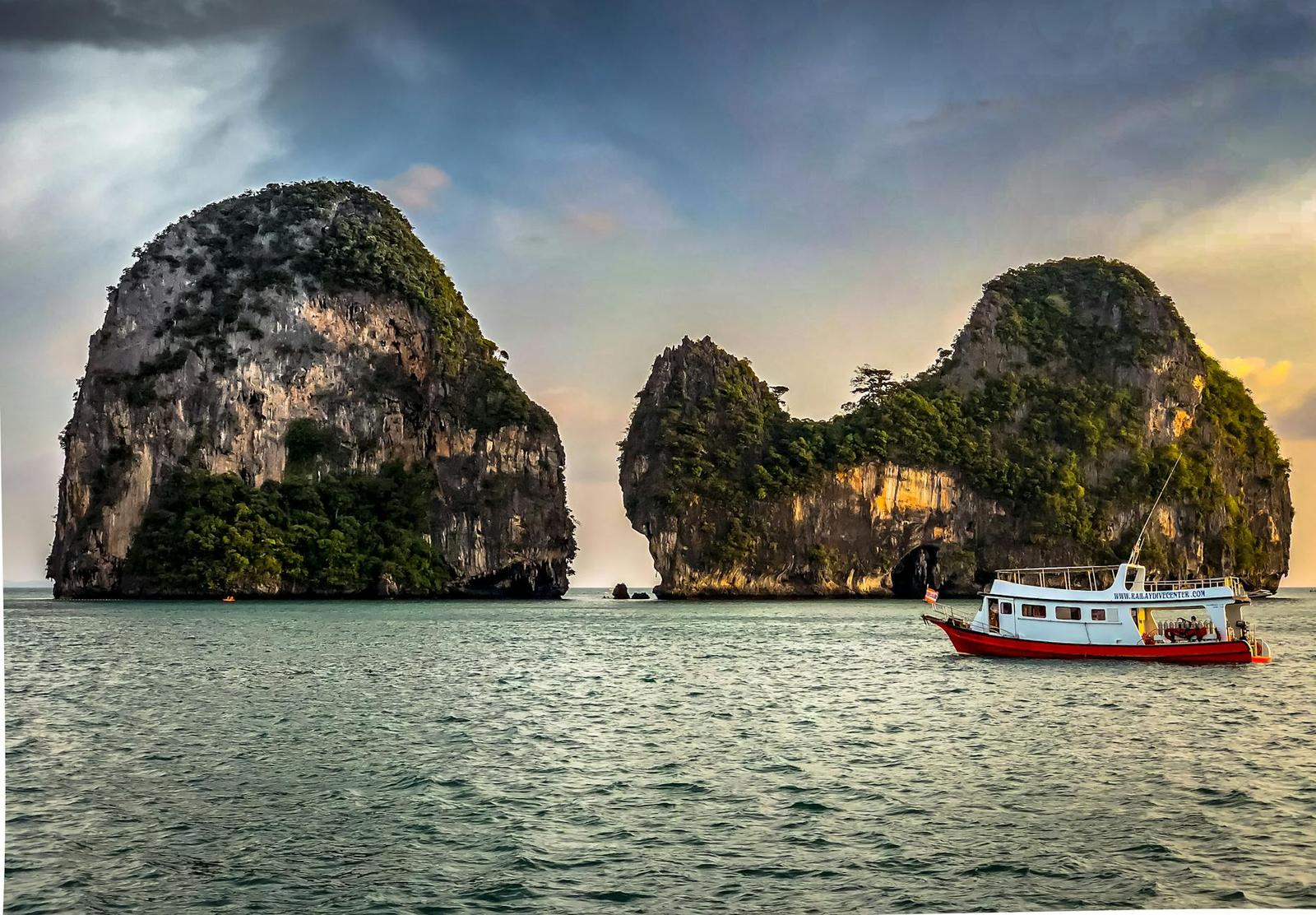 Fishing boat passing jagged limestone islets under a golden sky