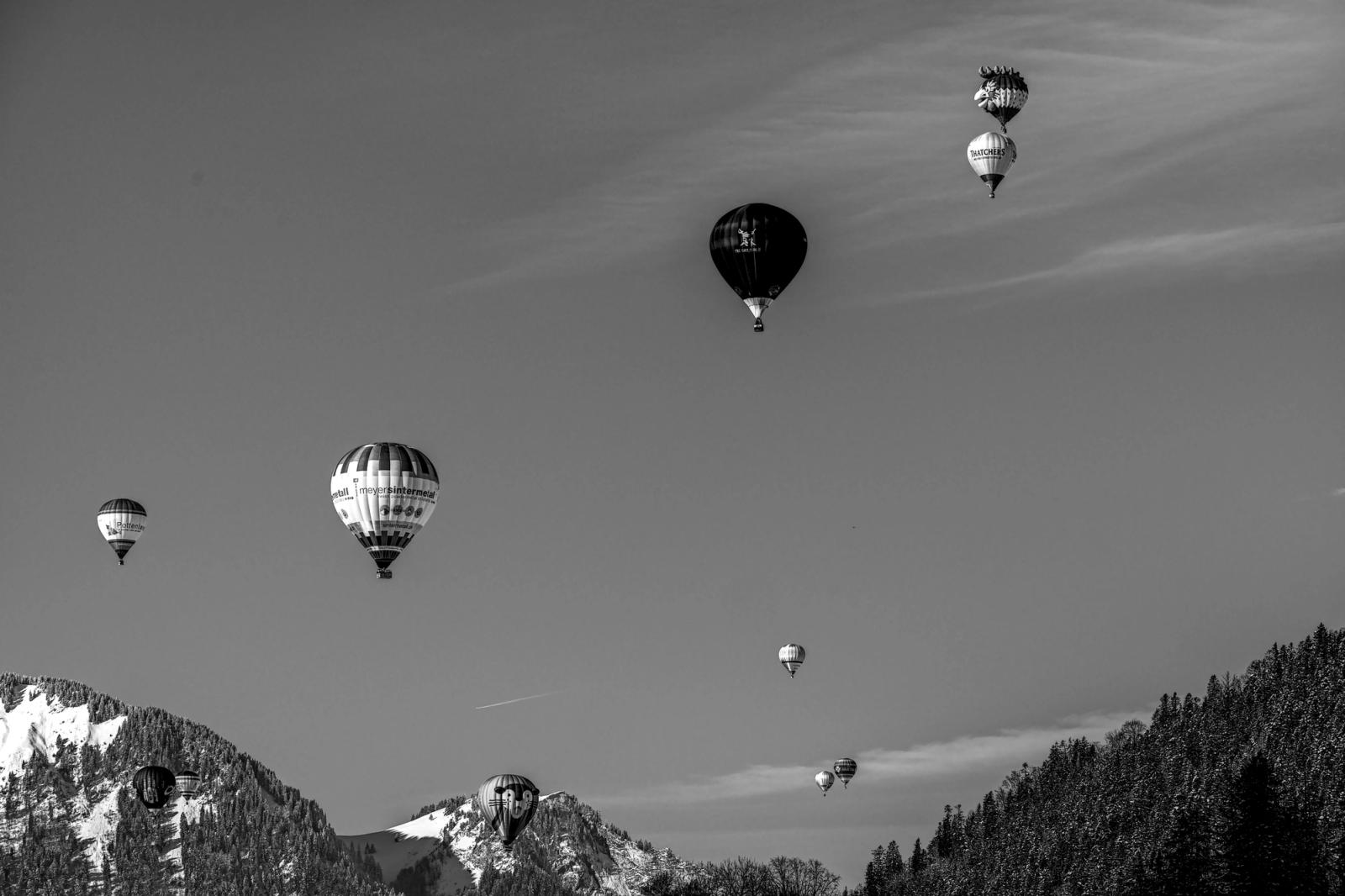 Black and white photo of hot air balloons soaring over the snow-capped Swiss Alps, creating a serene and adventurous scene