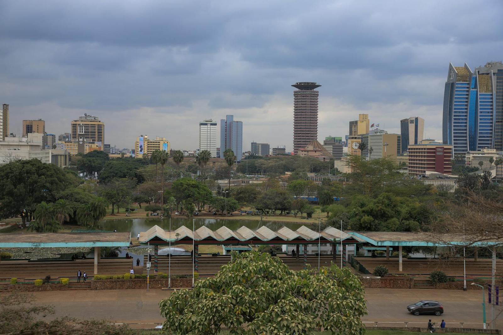 An overcast city skyline behind a canopied platform and green park