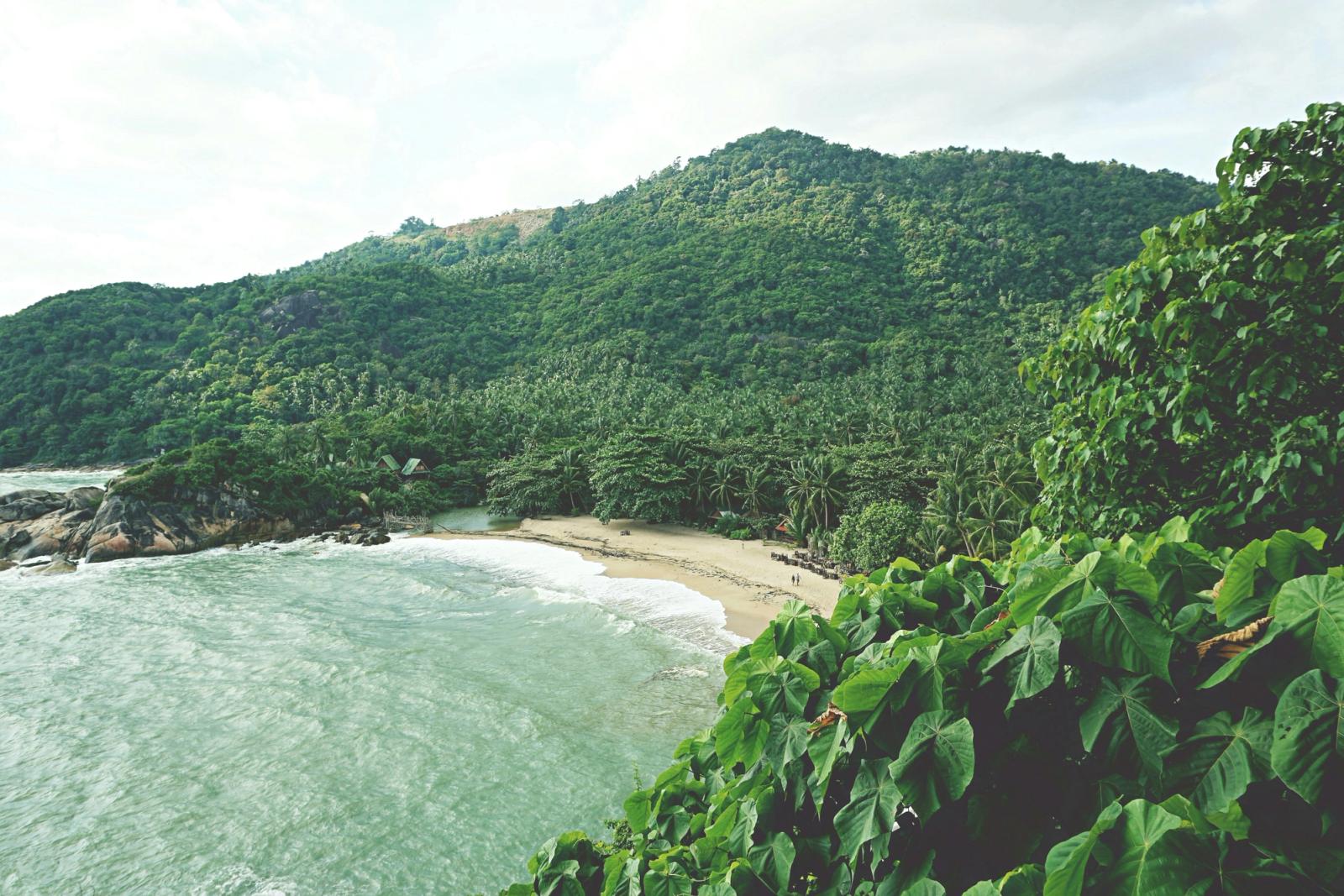 A picturesque tropical beach surrounded by lush green hills in Koh Phangan, Thailand