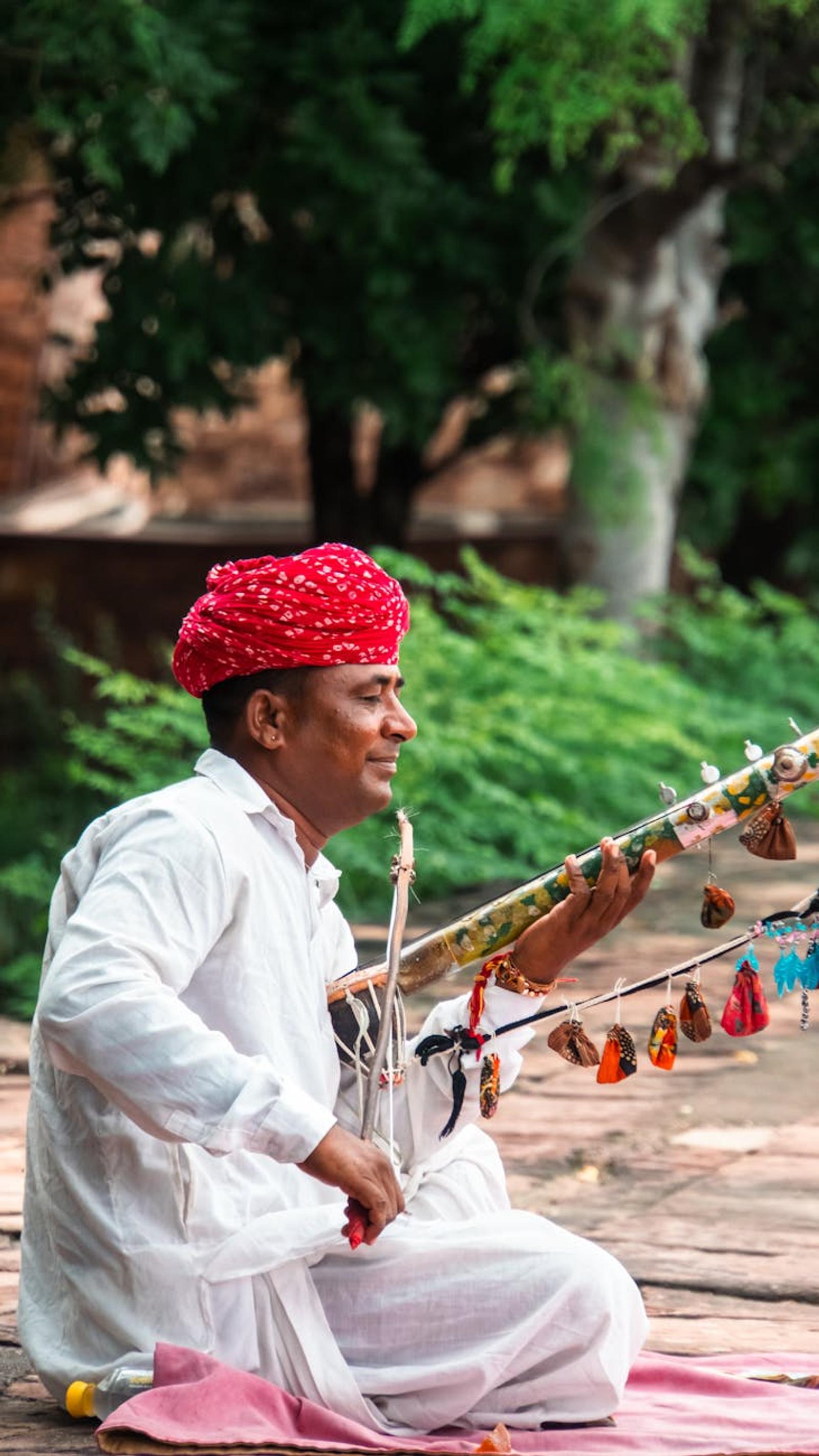 Indian musician in traditional attire playing an ethnic instrument outdoors