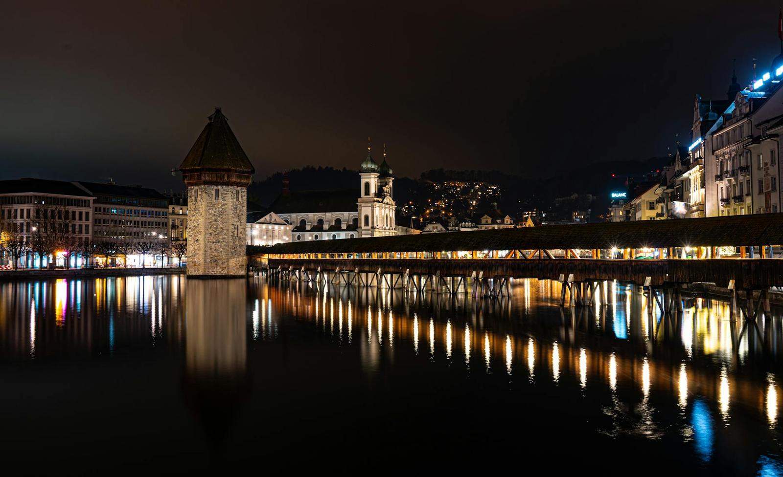 A lakeside wooden tower and covered bridge reflected in still water at night