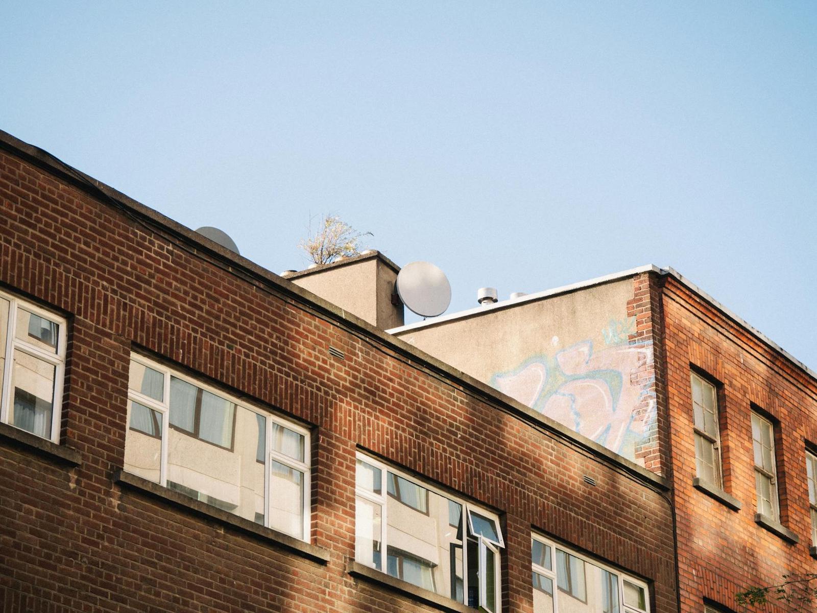 A weathered brick building rooftop with satellite dishes under a clear sky