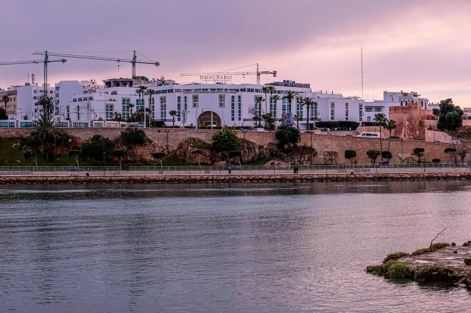 A large white waterfront building complex under a hazy pink evening sky