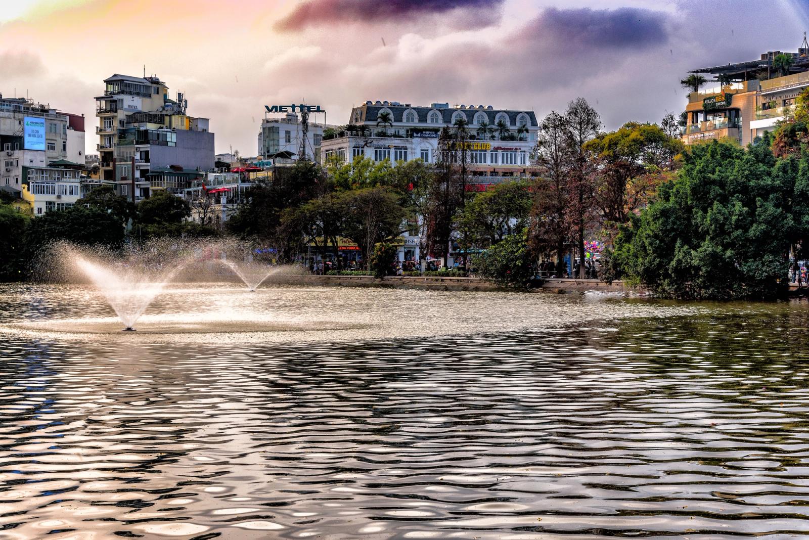 A scenic view of a pond and fountain in the urban landscape of Đống Đa, Hà Nội, Vietnam