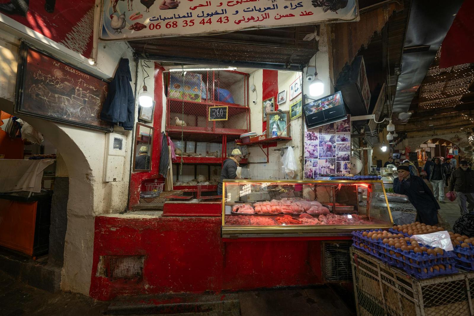 A butcher stall in a covered market with meat on display and crates of eggs